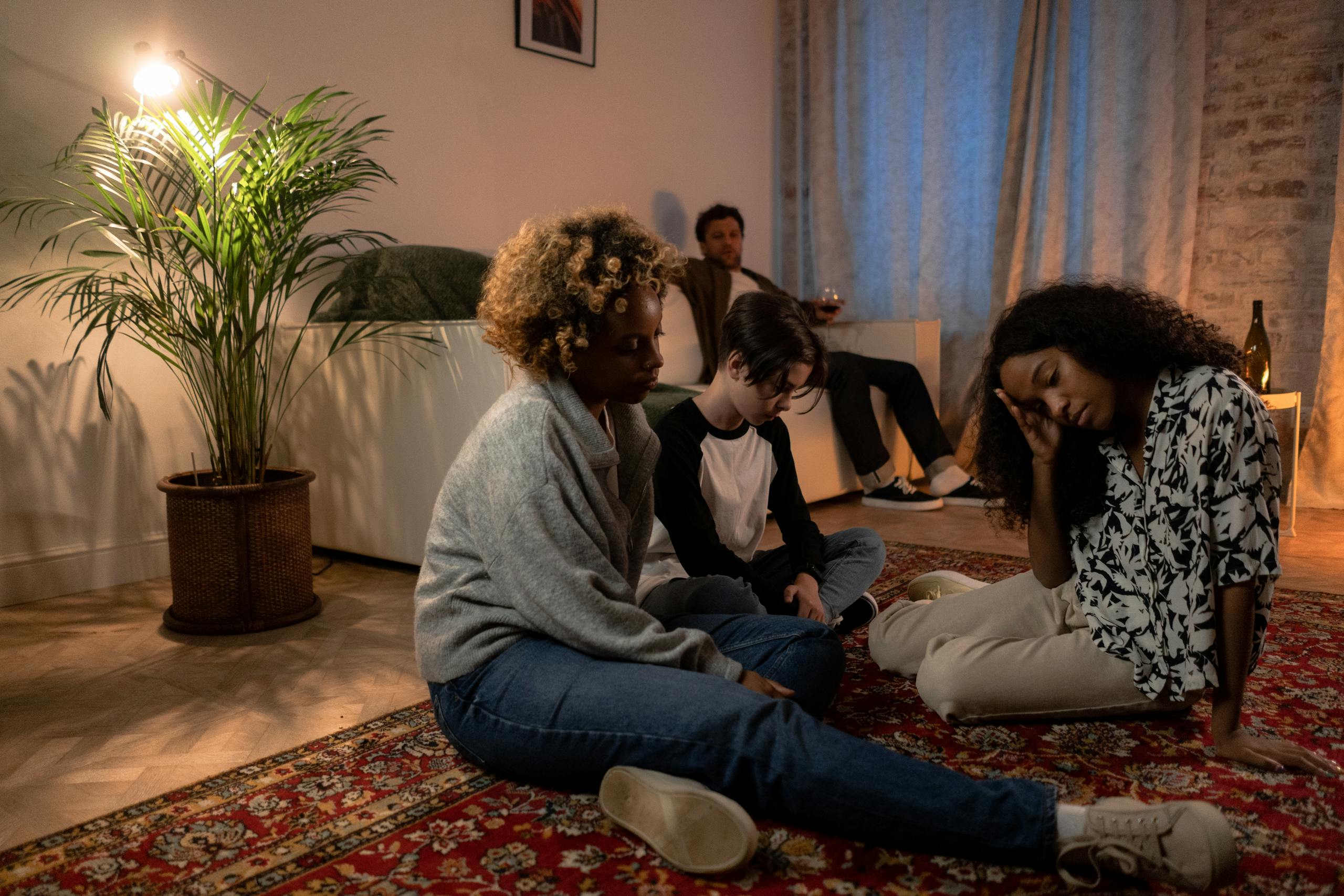 A group of adults showing concern and worry while sitting on a living room floor.