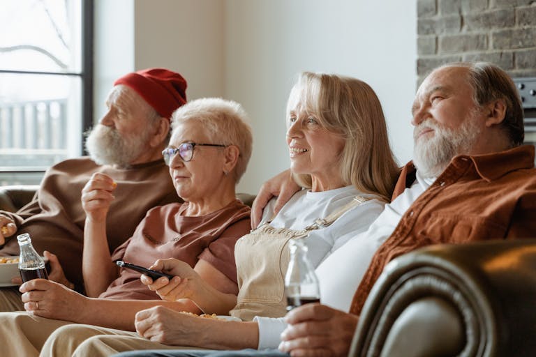 A group of senior adults sharing a cozy moment in a living room, enjoying snacks and drinks.