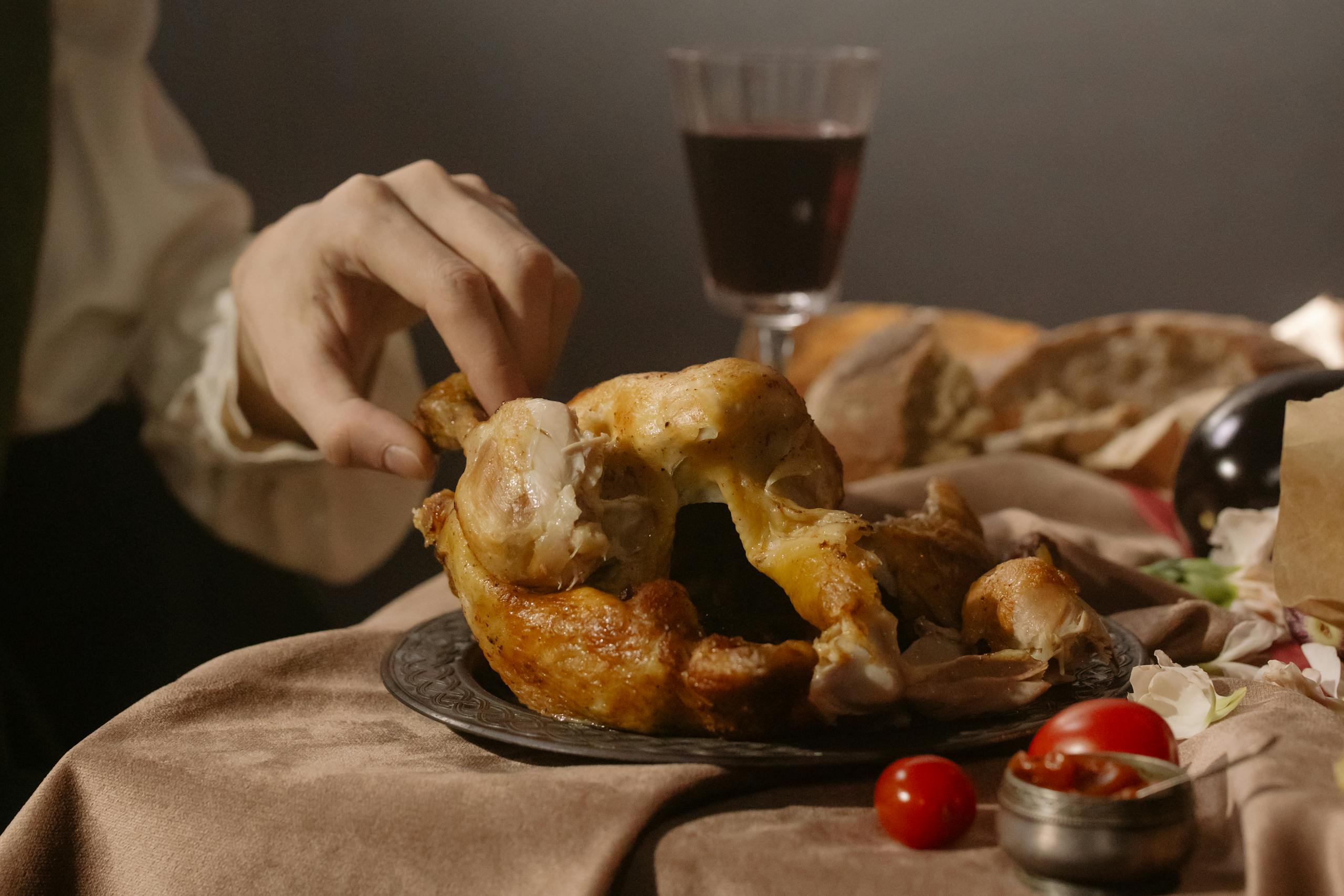 A hand reaches for succulent roast chicken on a Renaissance-style table setting.