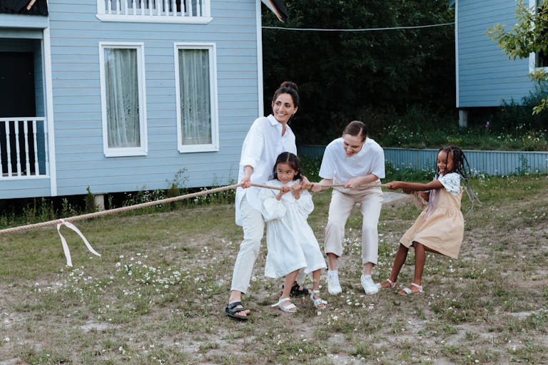 A happy family enjoys a game of tug of war in a grassy field by a house.