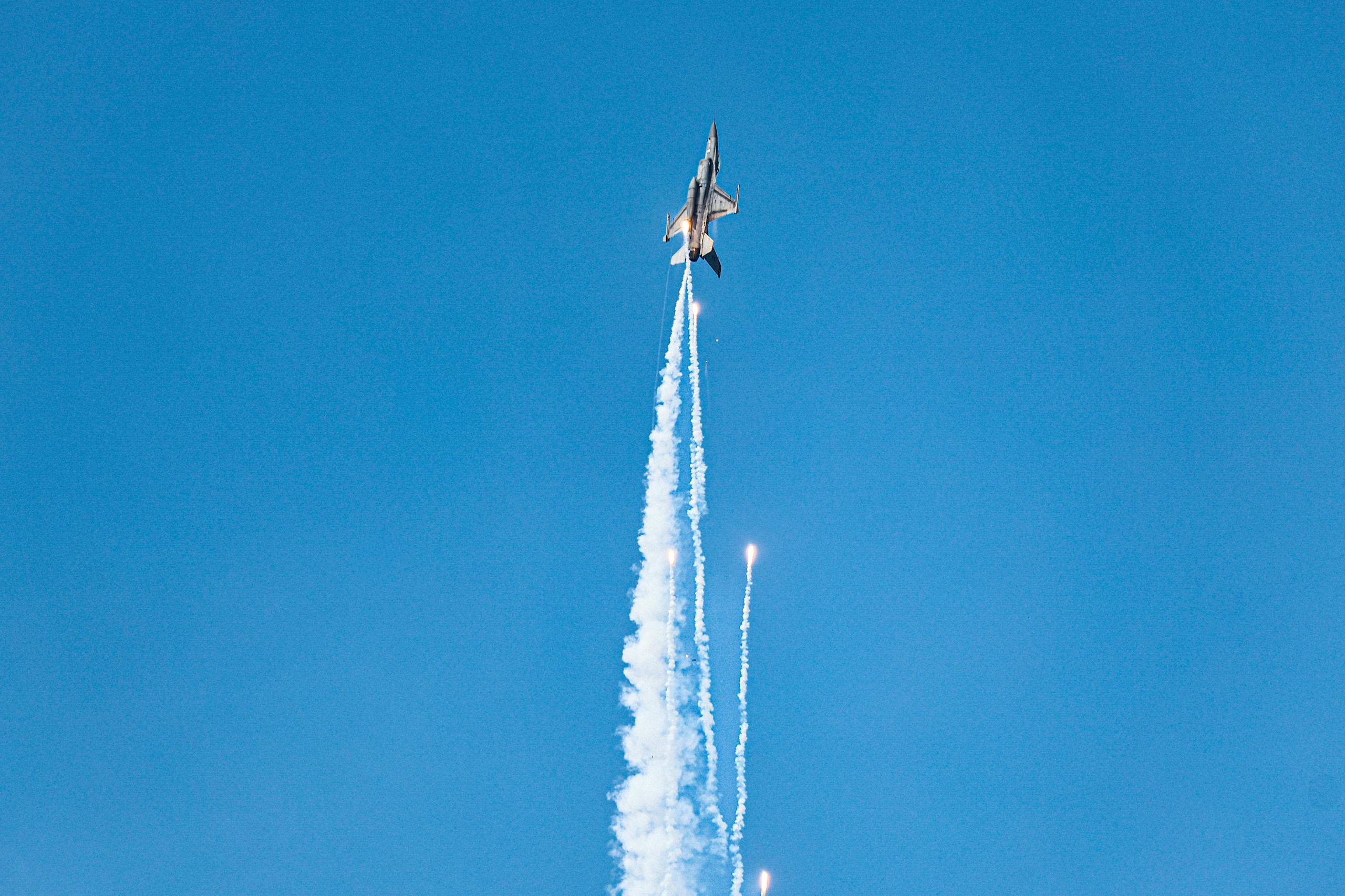A jet fighter performs a vertical ascent with smoke trails against a blue sky.
