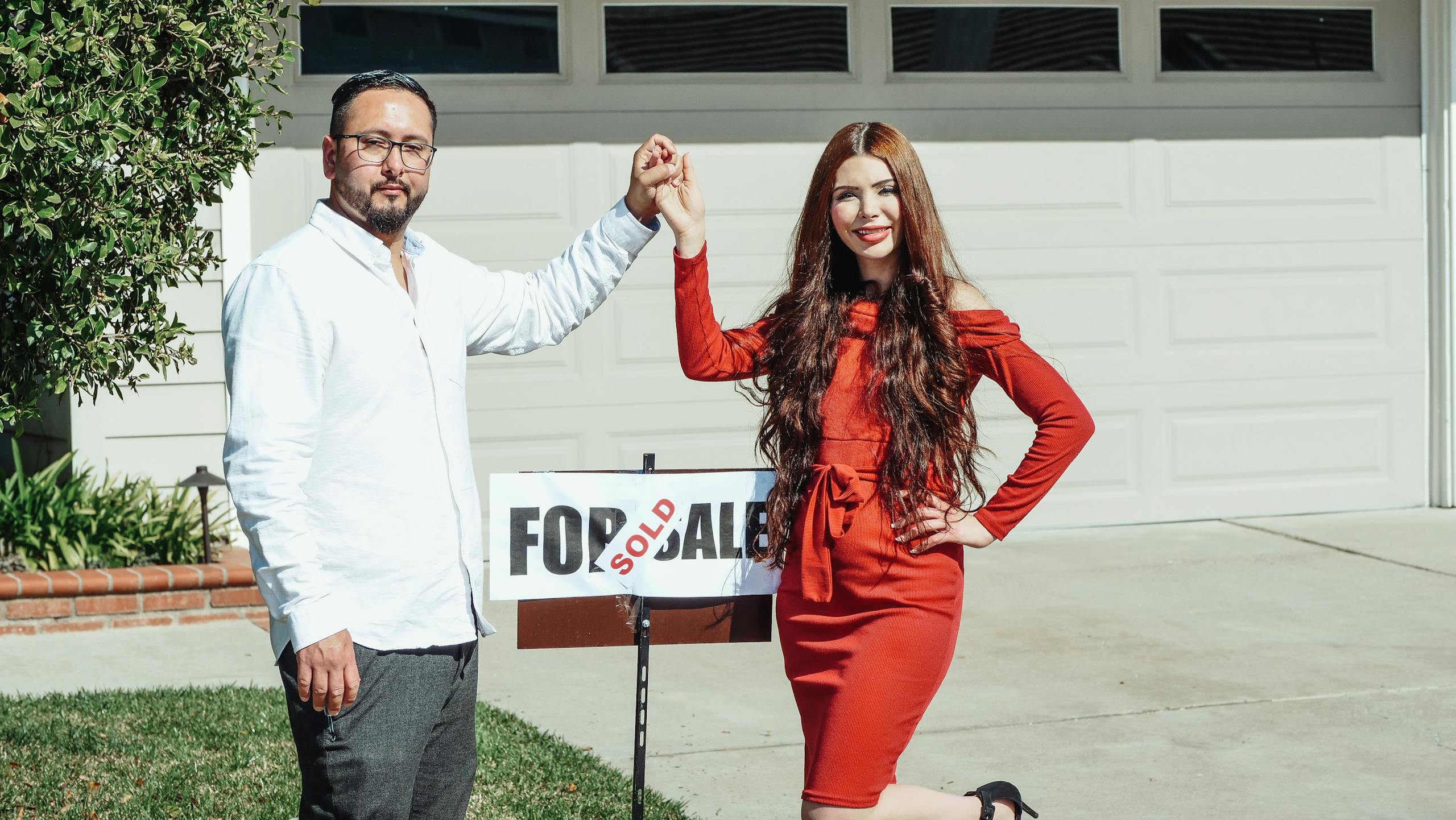 A joyful couple holding Sold sign in front of their new house, celebrating a home purchase.