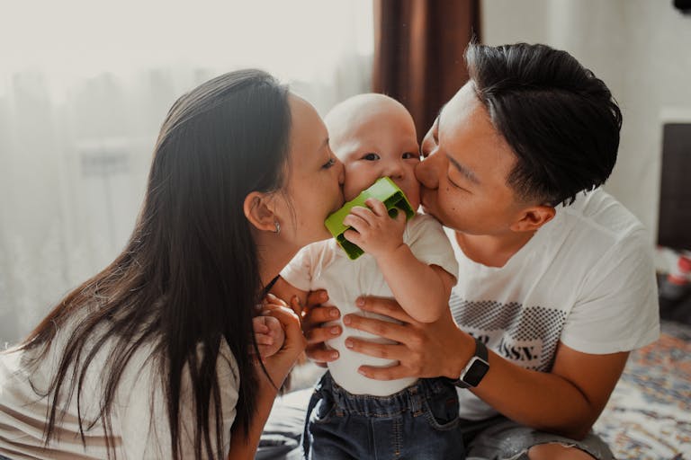 A joyful family scene with parents affectionately kissing their baby indoors, showcasing love and togetherness.
