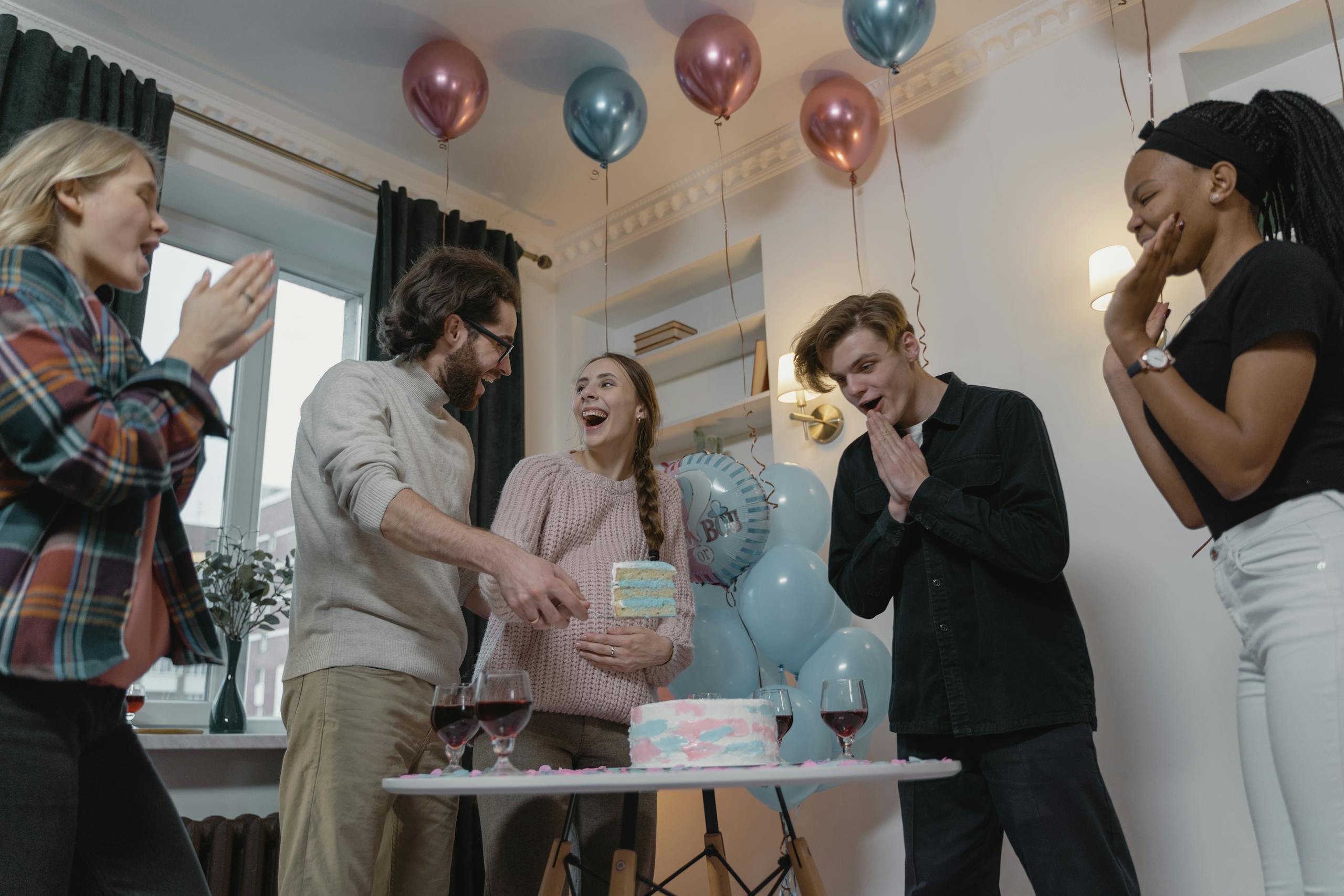 A joyful indoor gathering celebrating a gender reveal with cake and balloons.