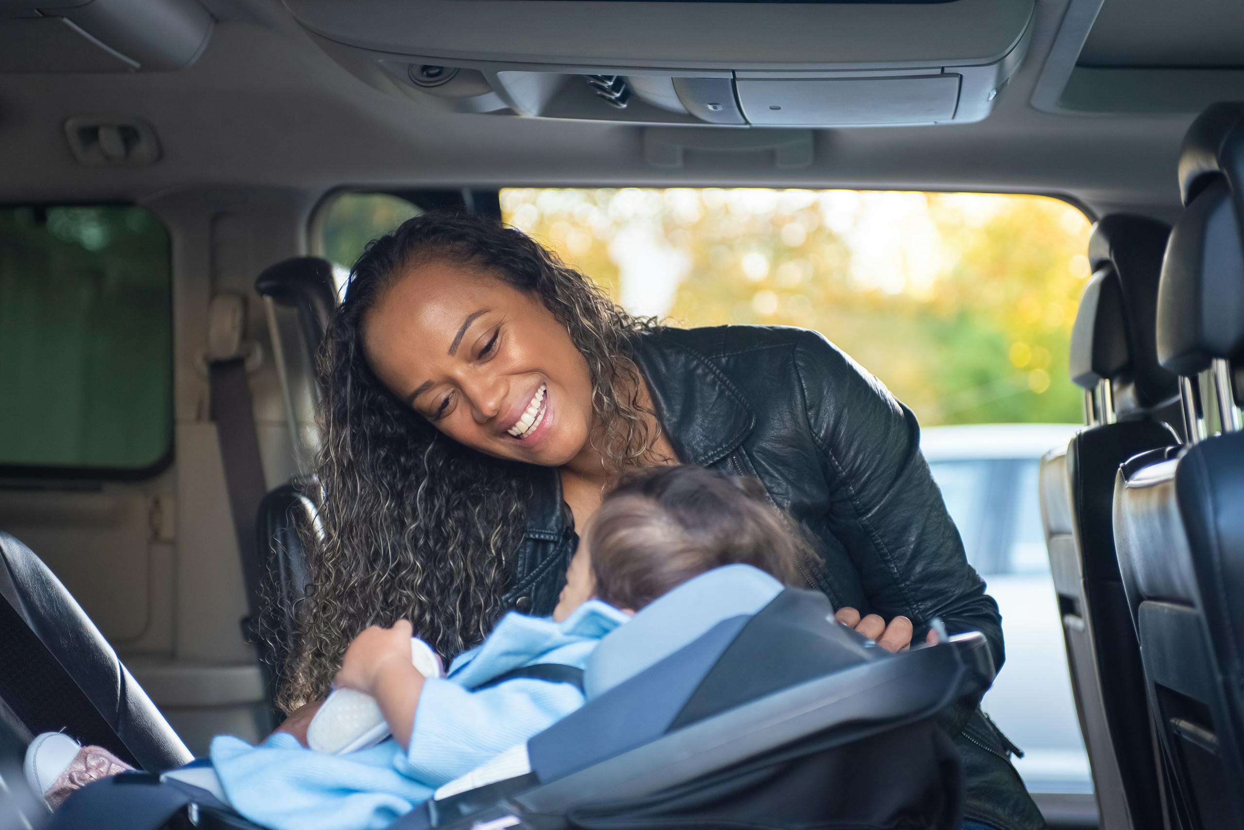 A joyful mother smiles at her baby in a car seat inside a vehicle.