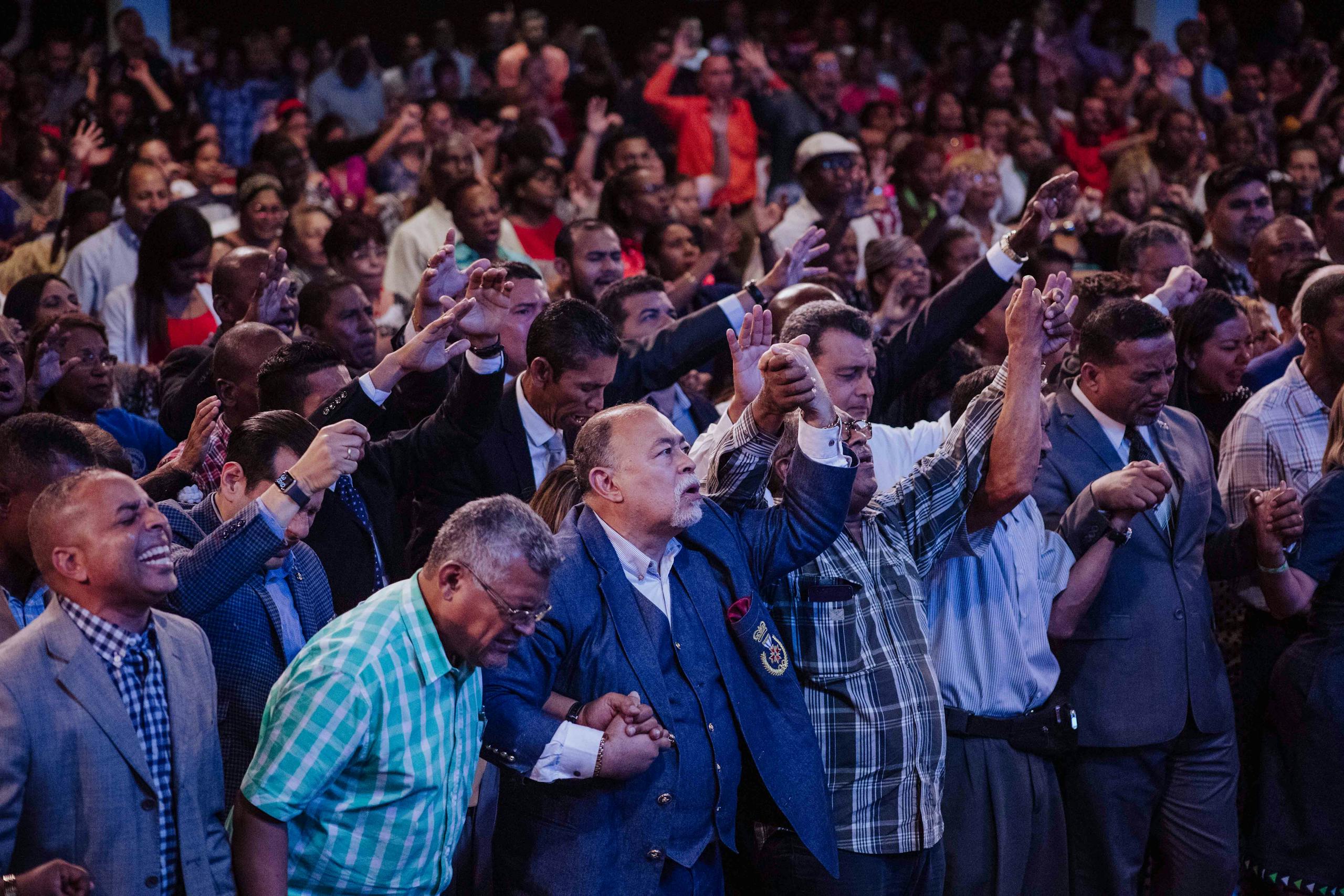 A large, diverse group of adults holding hands in a spiritual worship gathering.