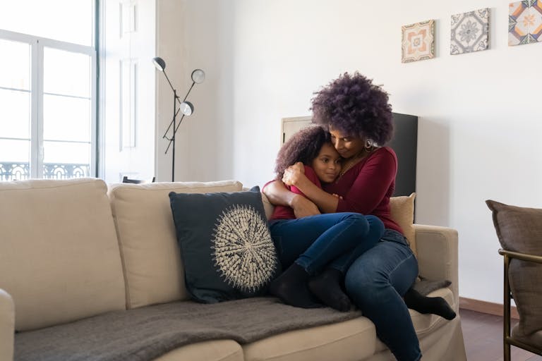 A loving mother embraces her daughter on a cozy sofa at home, creating a warm and affectionate family moment.