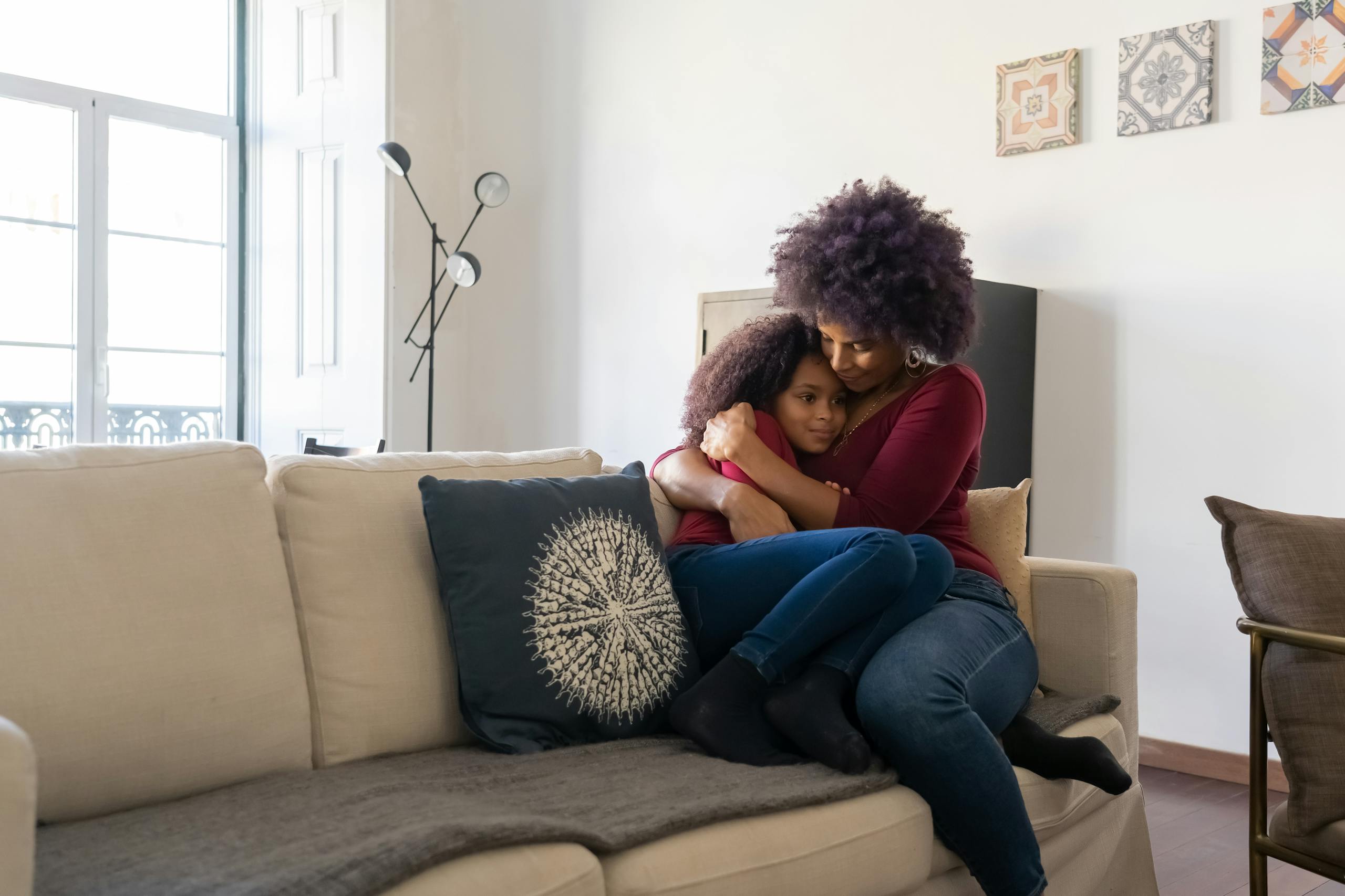 A loving mother embraces her daughter on a cozy sofa at home, creating a warm and affectionate family moment.