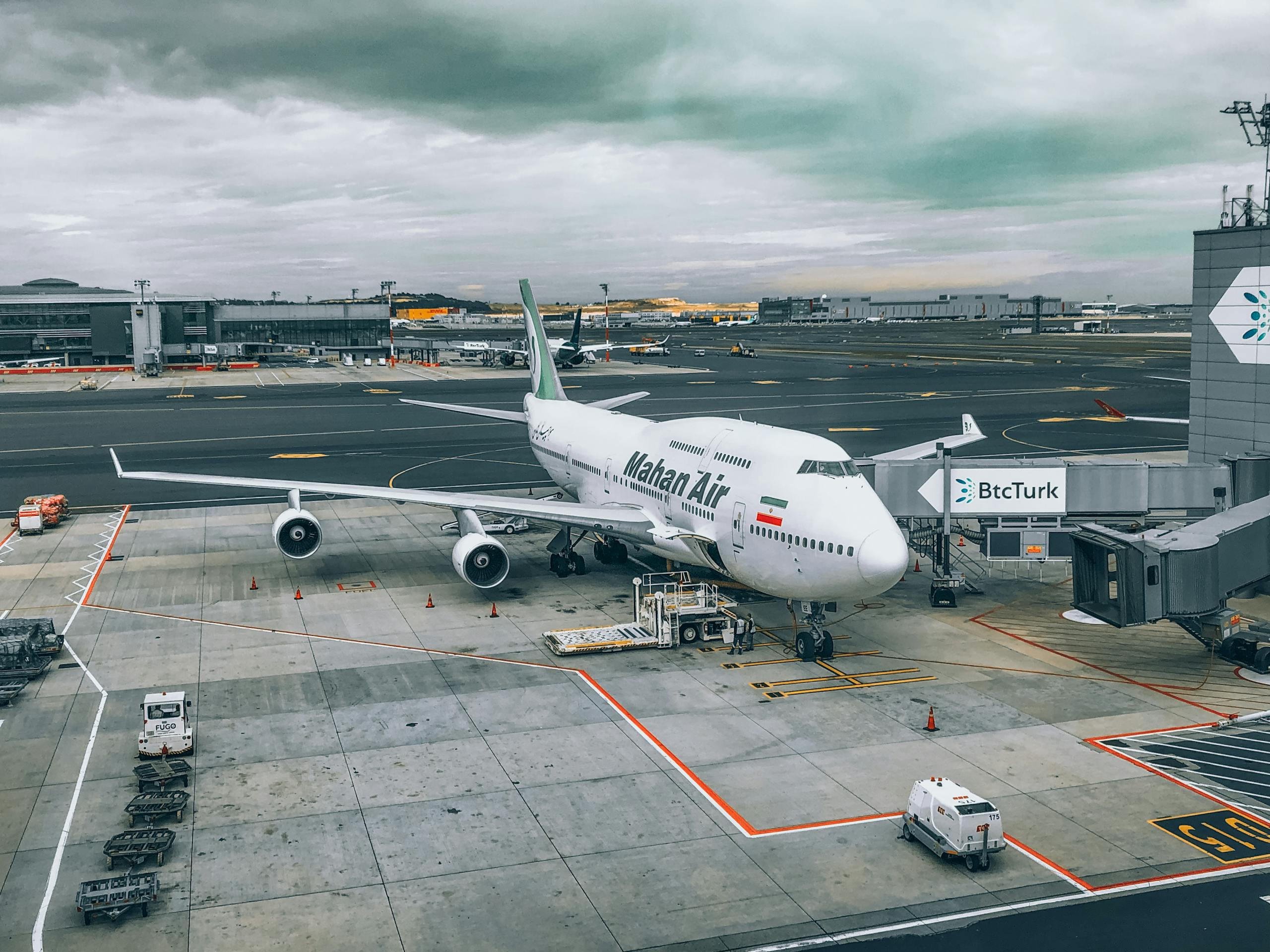 A Mahan Air Boeing 747 aircraft parked at a bustling airport terminal under cloudy skies.