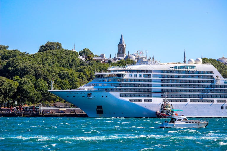 A majestic cruise ship sails through the Bosphorus Strait with a historic Istanbul skyline in the backdrop.