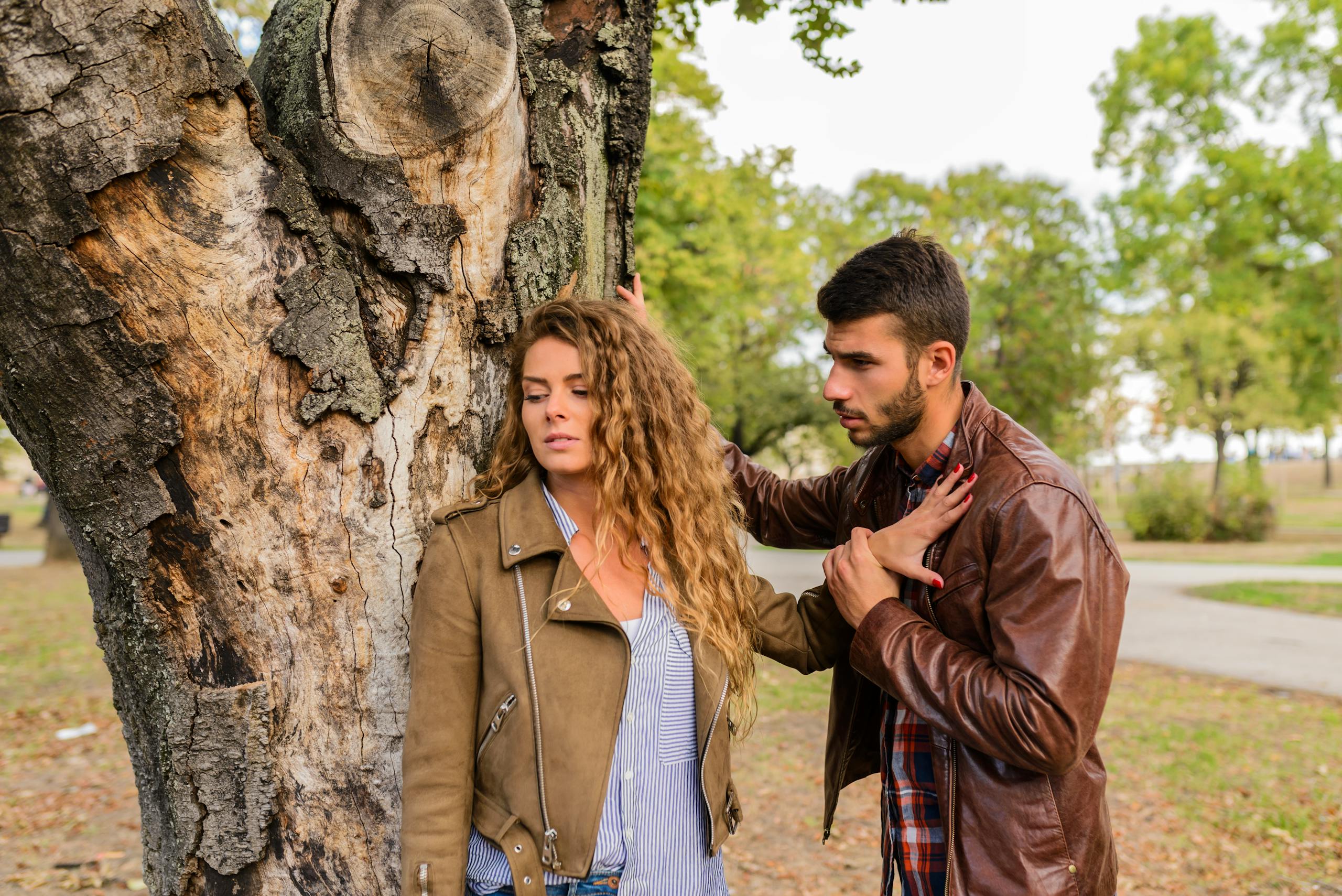 A man and a woman in an emotional conversation by a tree in a park.