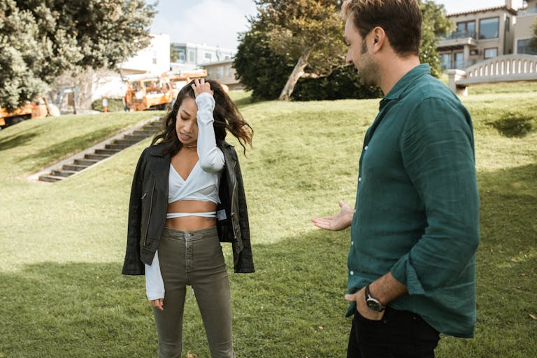 A man and woman engage in a casual conversation in a sunny park setting.