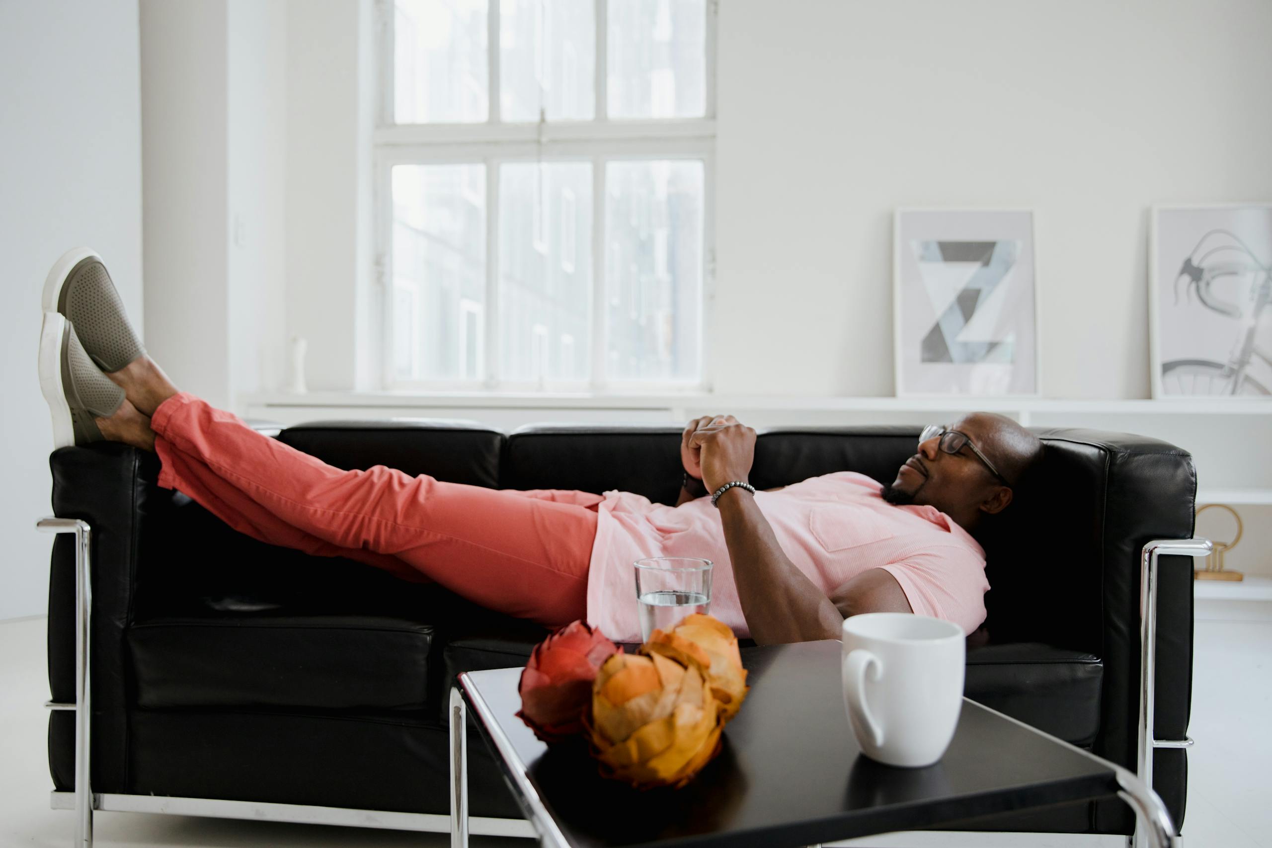A man comfortably lounging on a black sofa in a bright room with modern decor.