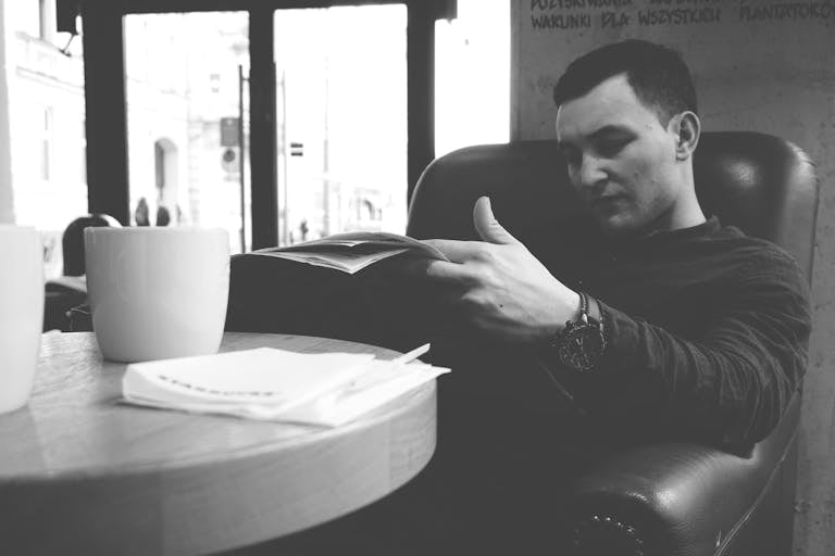 A man sits comfortably in a cafe chair reading a newspaper. Monochrome style.