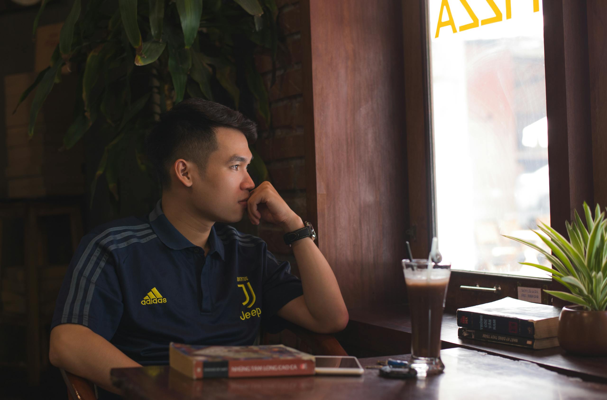 A man thoughtfully gazing outside a cozy restaurant window with a coffee on the table.