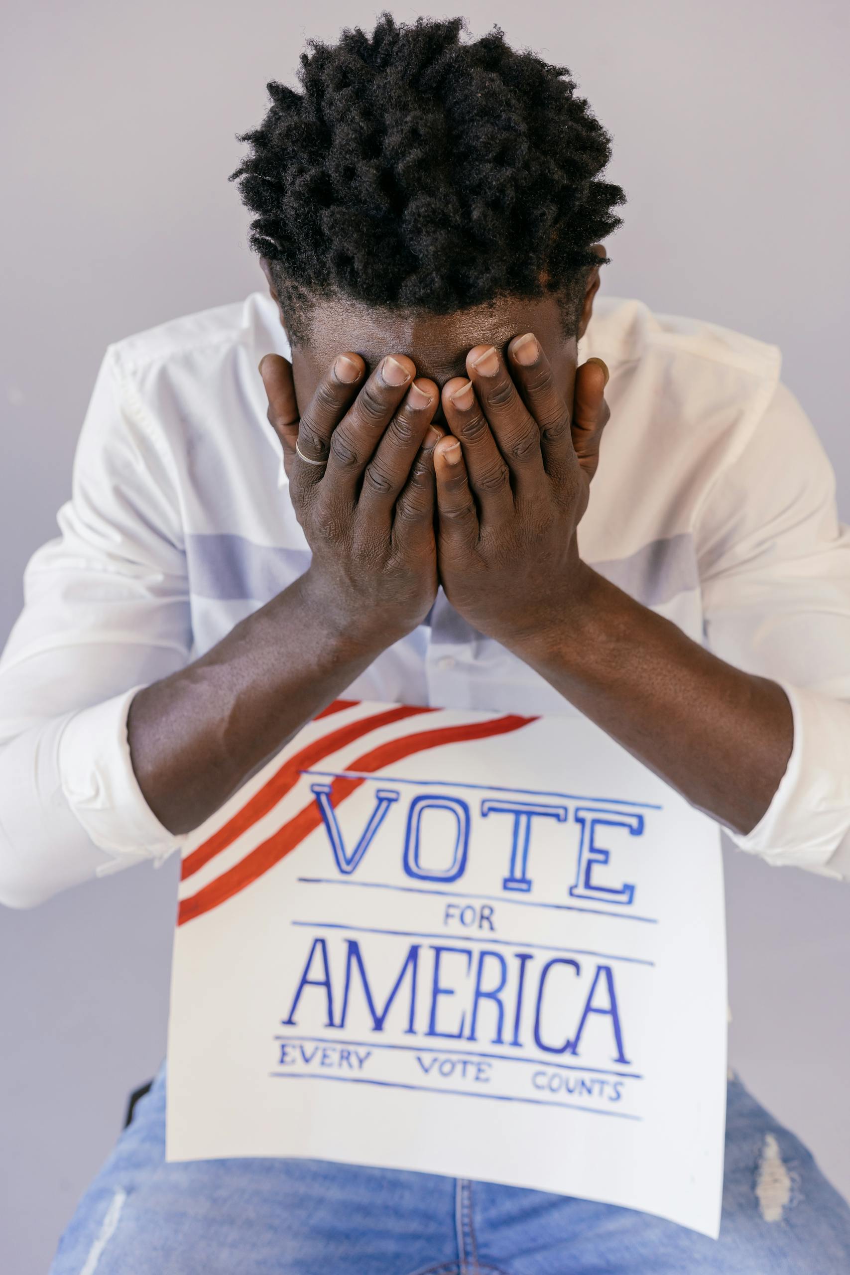 A man with a political sign covers his face, conveying emotions around voting.