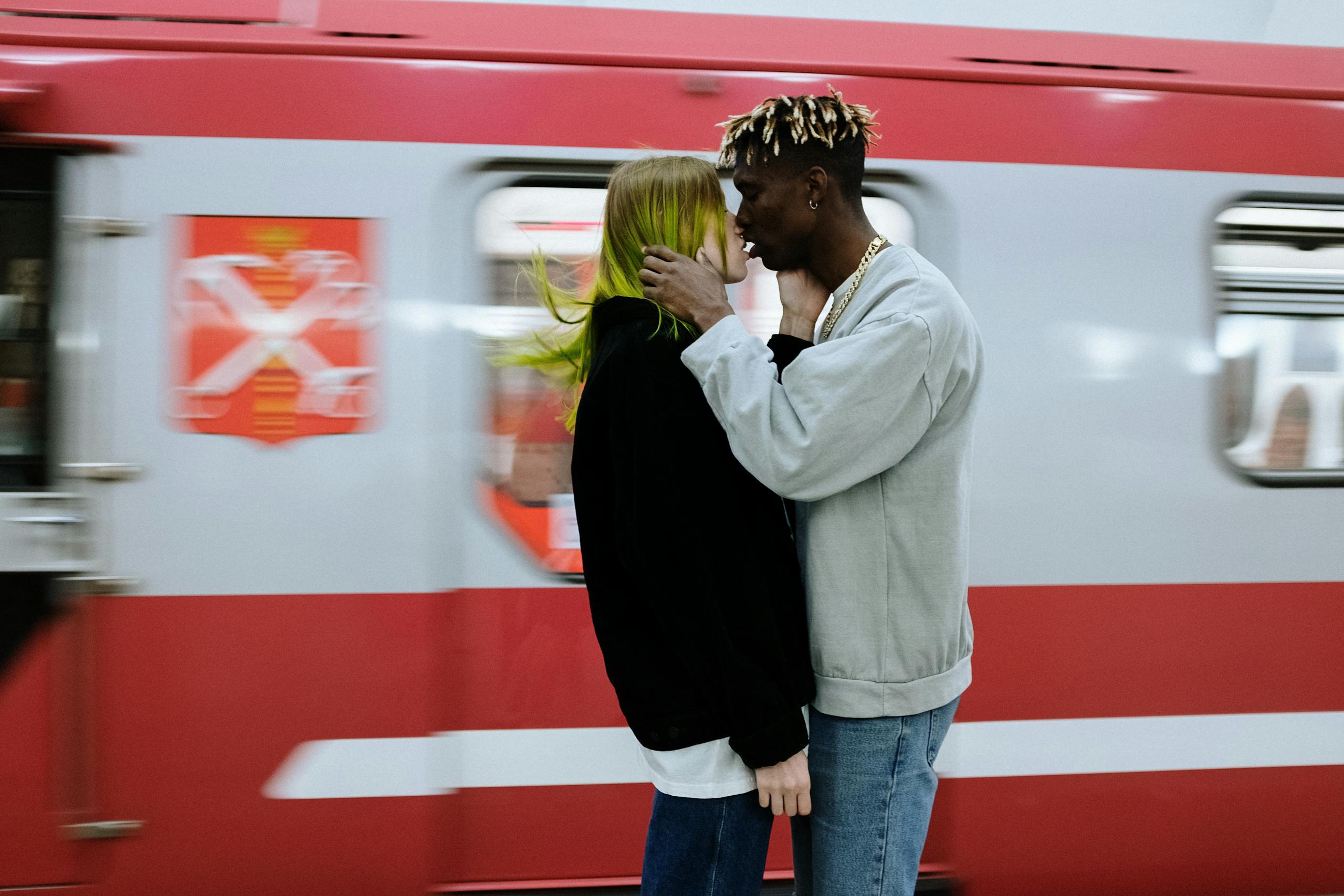 A modern couple shares a romantic moment at a bustling subway platform, capturing the essence of urban life.