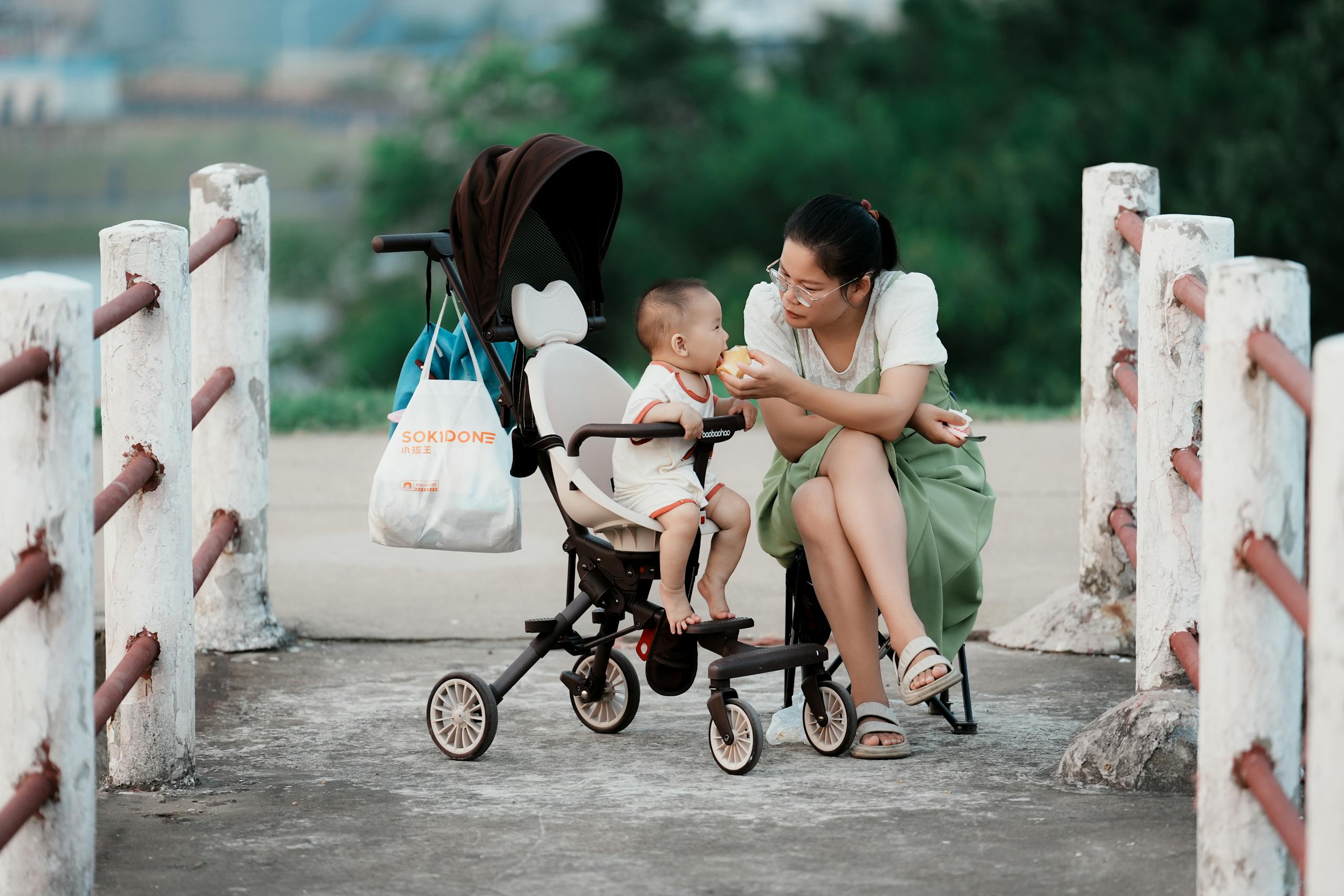 A mother lovingly feeds her baby while sitting outdoors with a stroller.