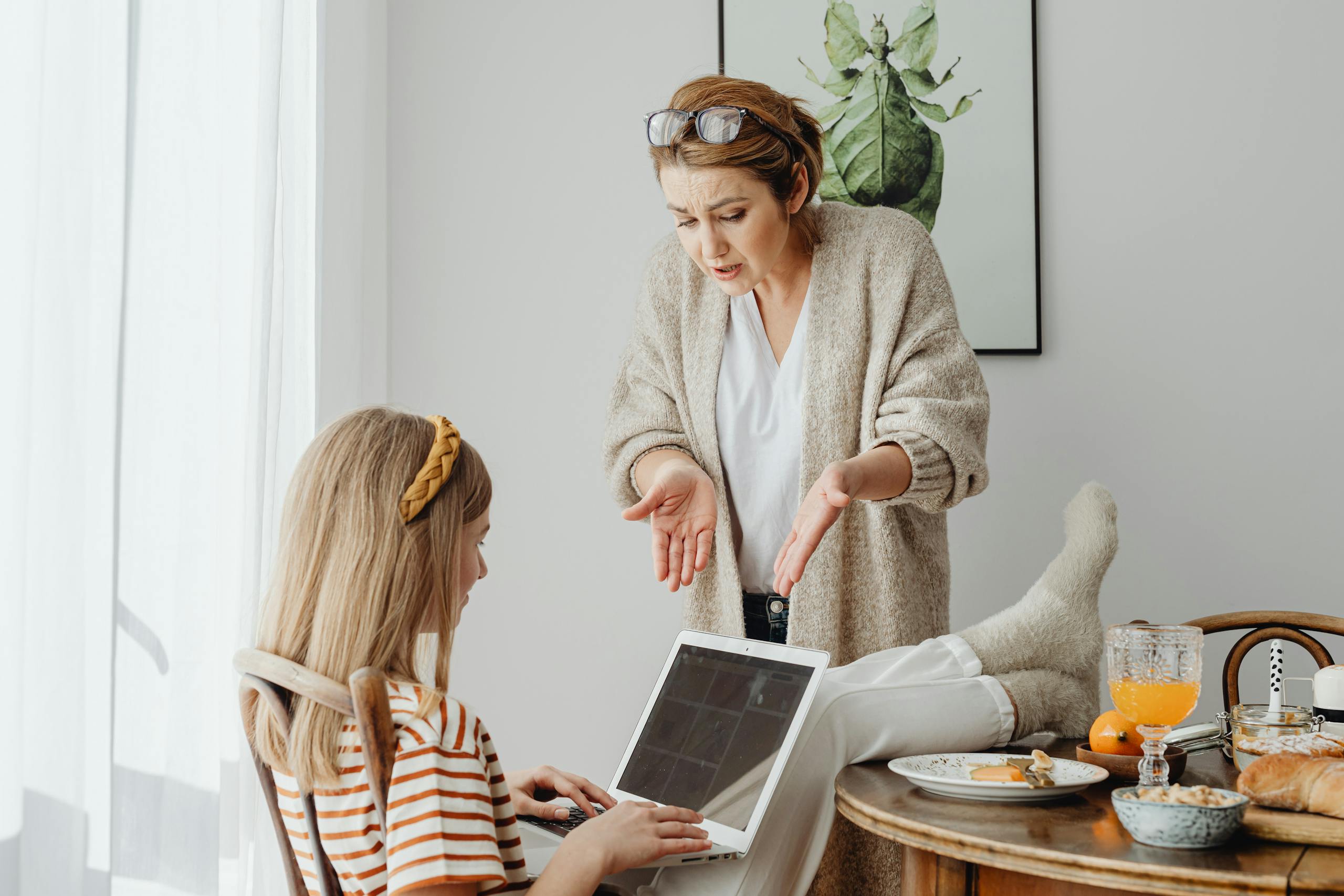 A mother scolds her teenage daughter absorbed in her laptop during breakfast at home.