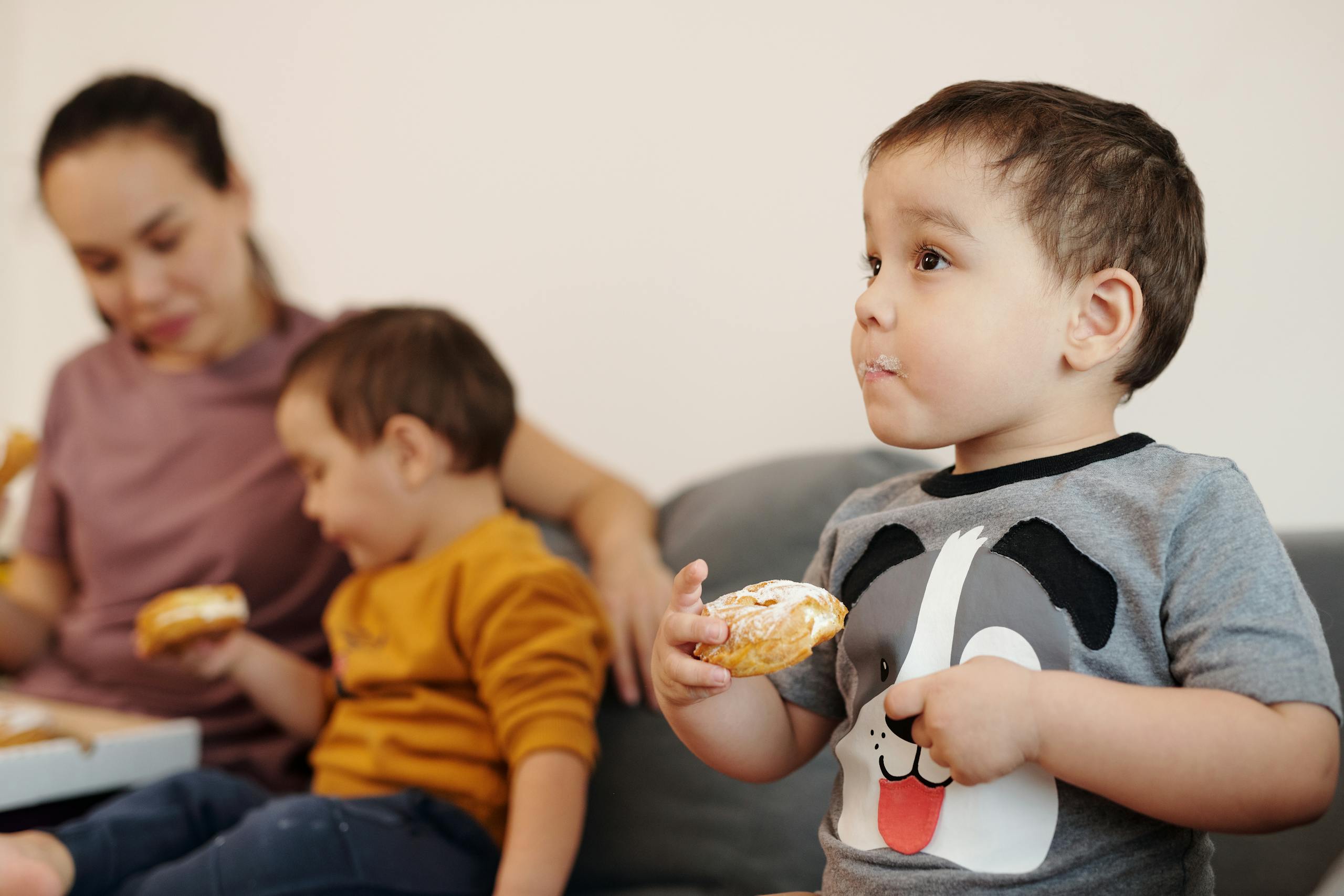 A mother sitting with her two young sons enjoying donuts together indoors.