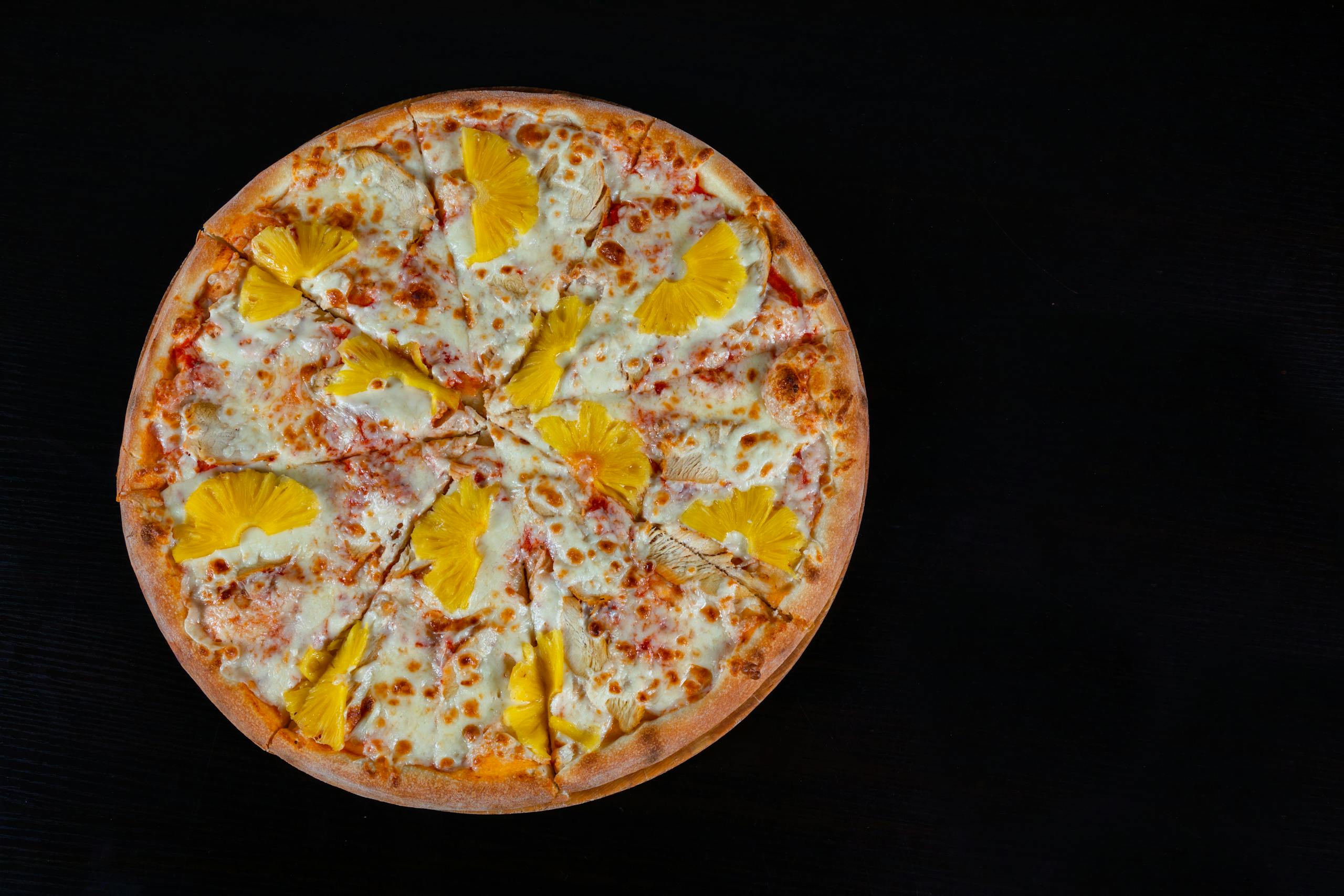 A mouthwatering Hawaiian pizza topped with cheese and pineapple on a dark background.