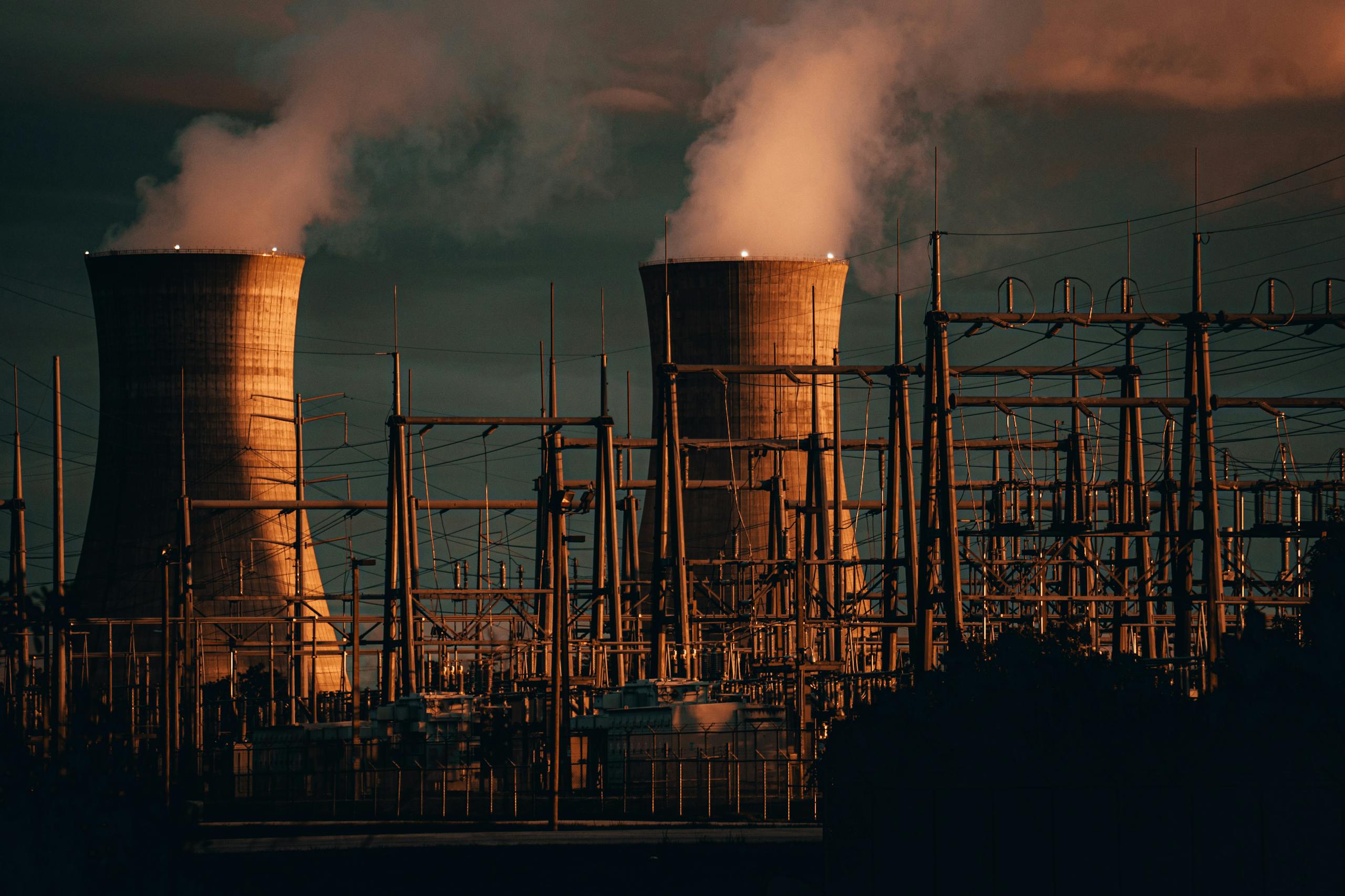 A nuclear power plant's cooling towers emit steam at sunset, highlighting industrial infrastructure.