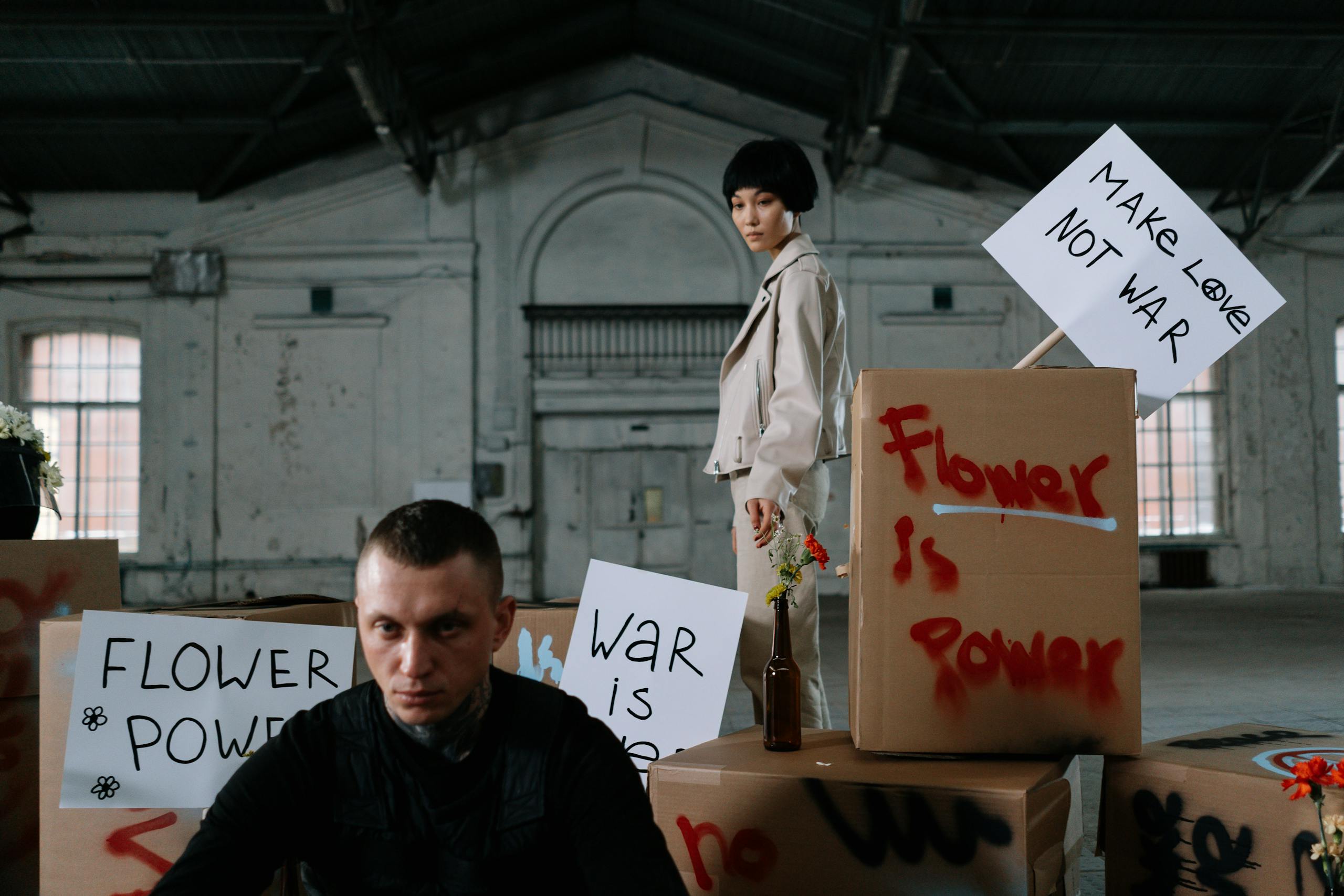 A peaceful indoor protest features activists with signs promoting nonviolence, including 'Flower is Power.'