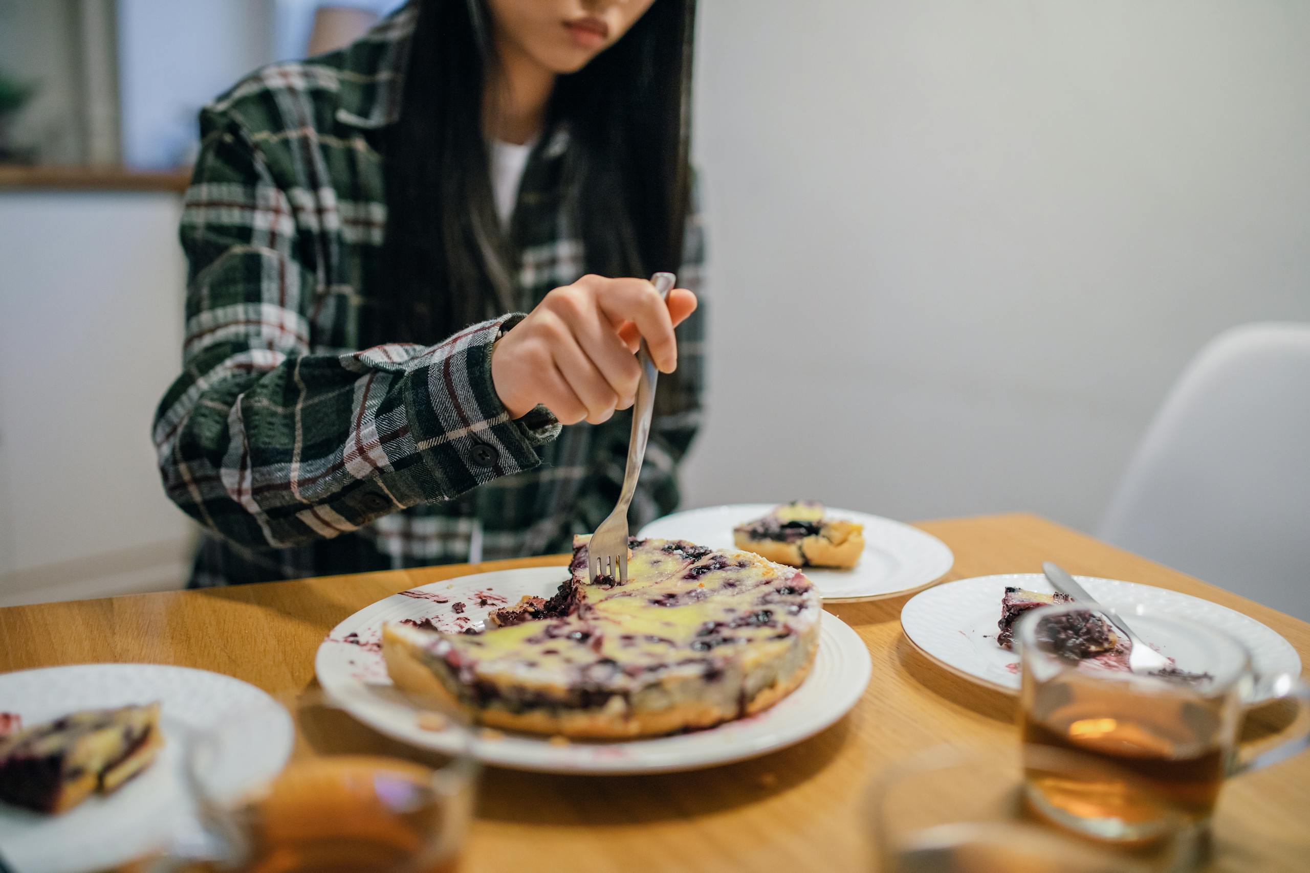 A person cuts a slice of homemade berry pie at a dining table, creating a cozy and inviting atmosphere.