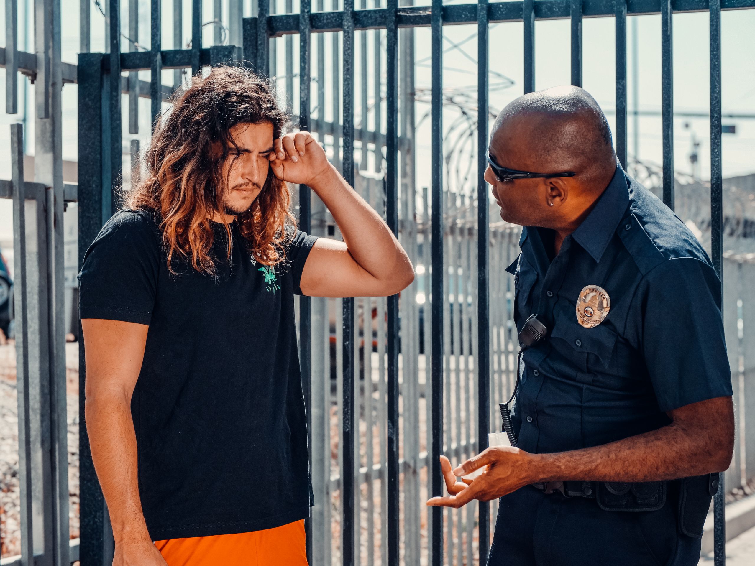 A police officer engages in a serious conversation with a civilian outdoors near a fence.