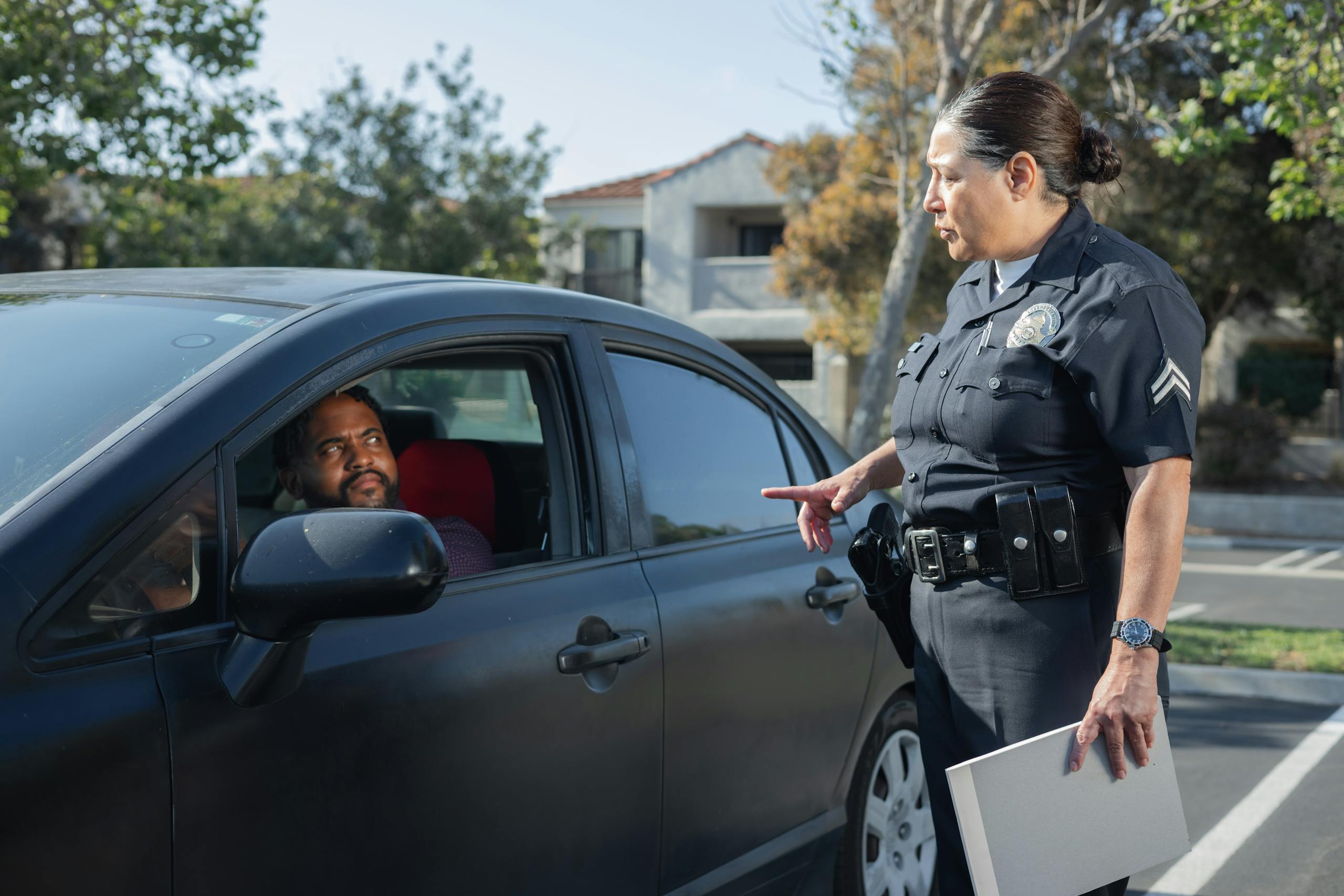 A police officer interacts with a driver during a daytime traffic stop on a residential street.
