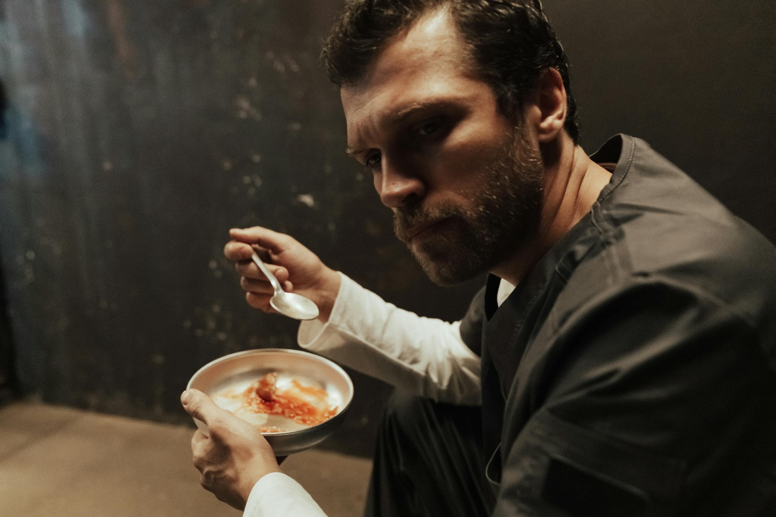 A prisoner in a dark cell eating a simple meal, conveying solitude and introspection.