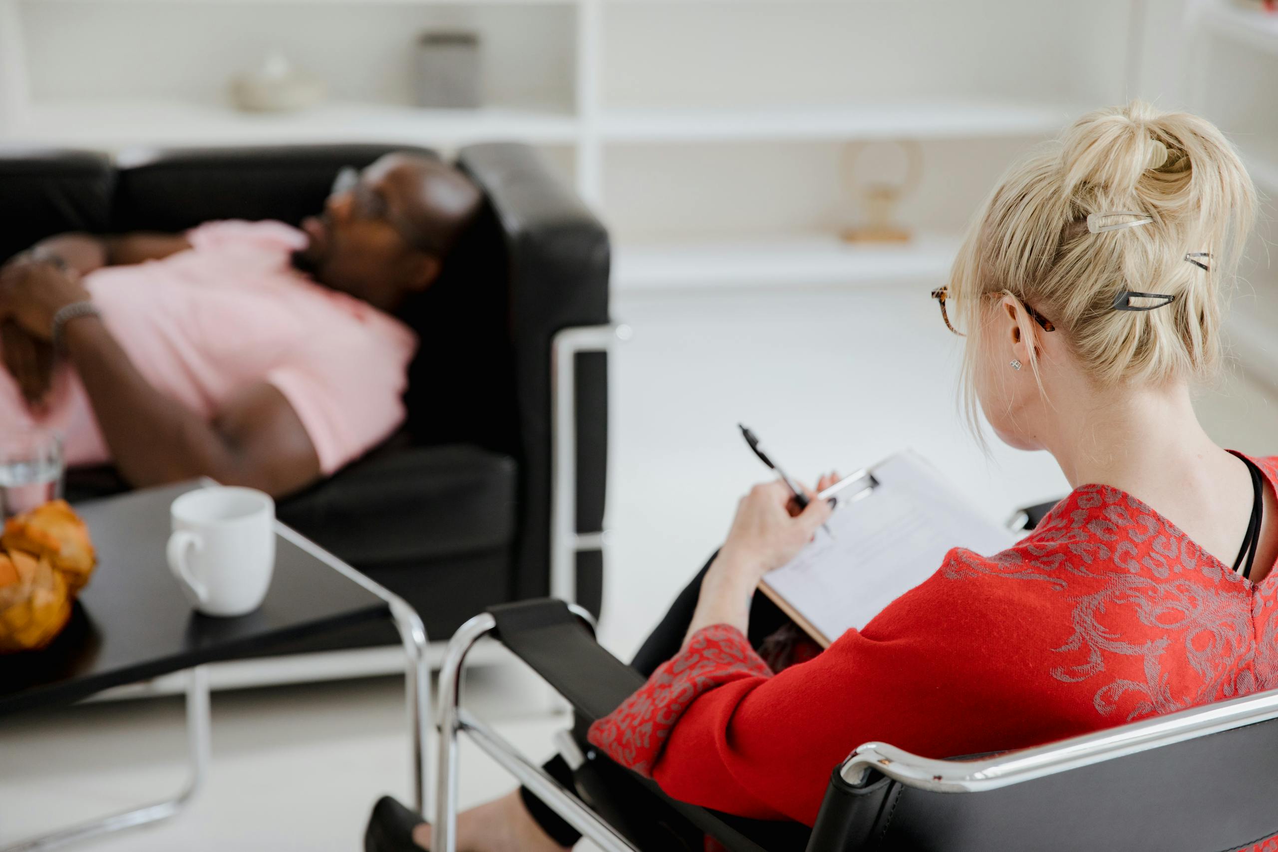 A professional therapist takes notes during a therapy session, engaging with a client.
