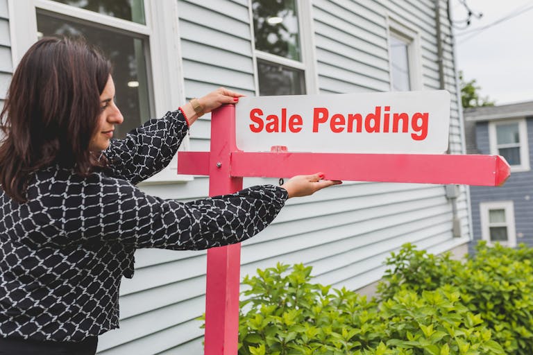 A realtor is adjusting a sale pending sign outside a house for sale.