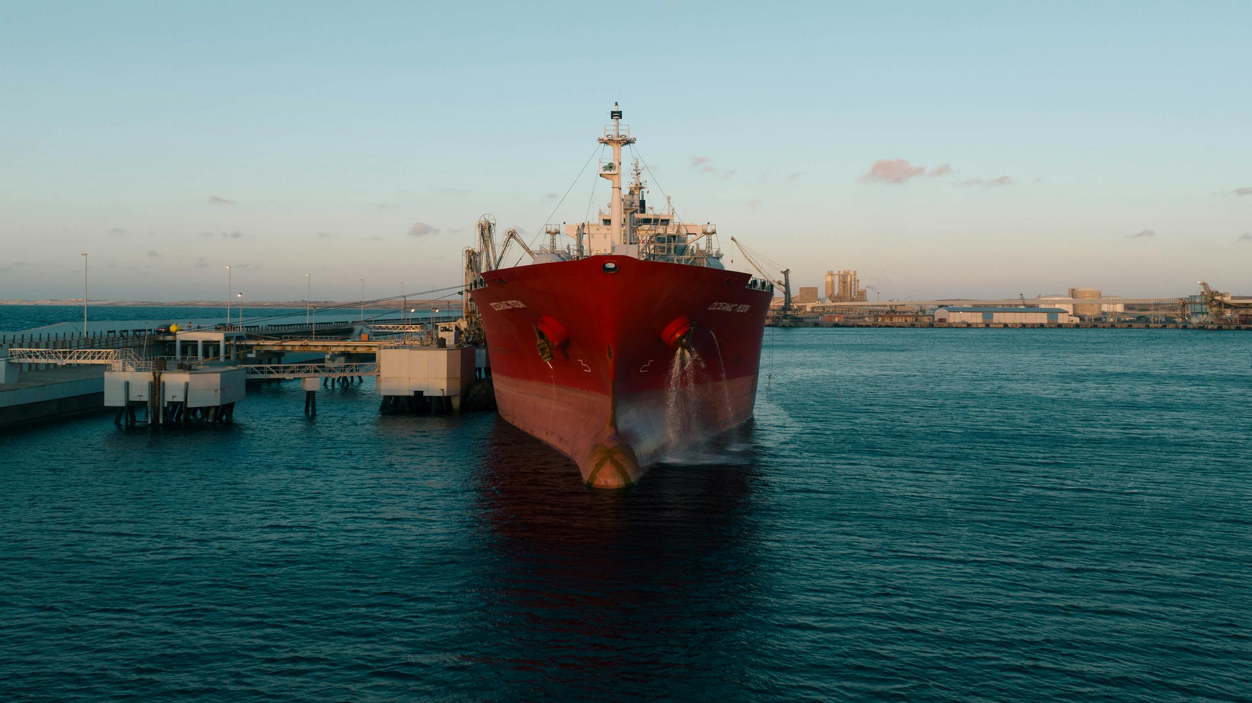 A red cargo ship docked at an industrial port during sunset, capturing maritime trade.