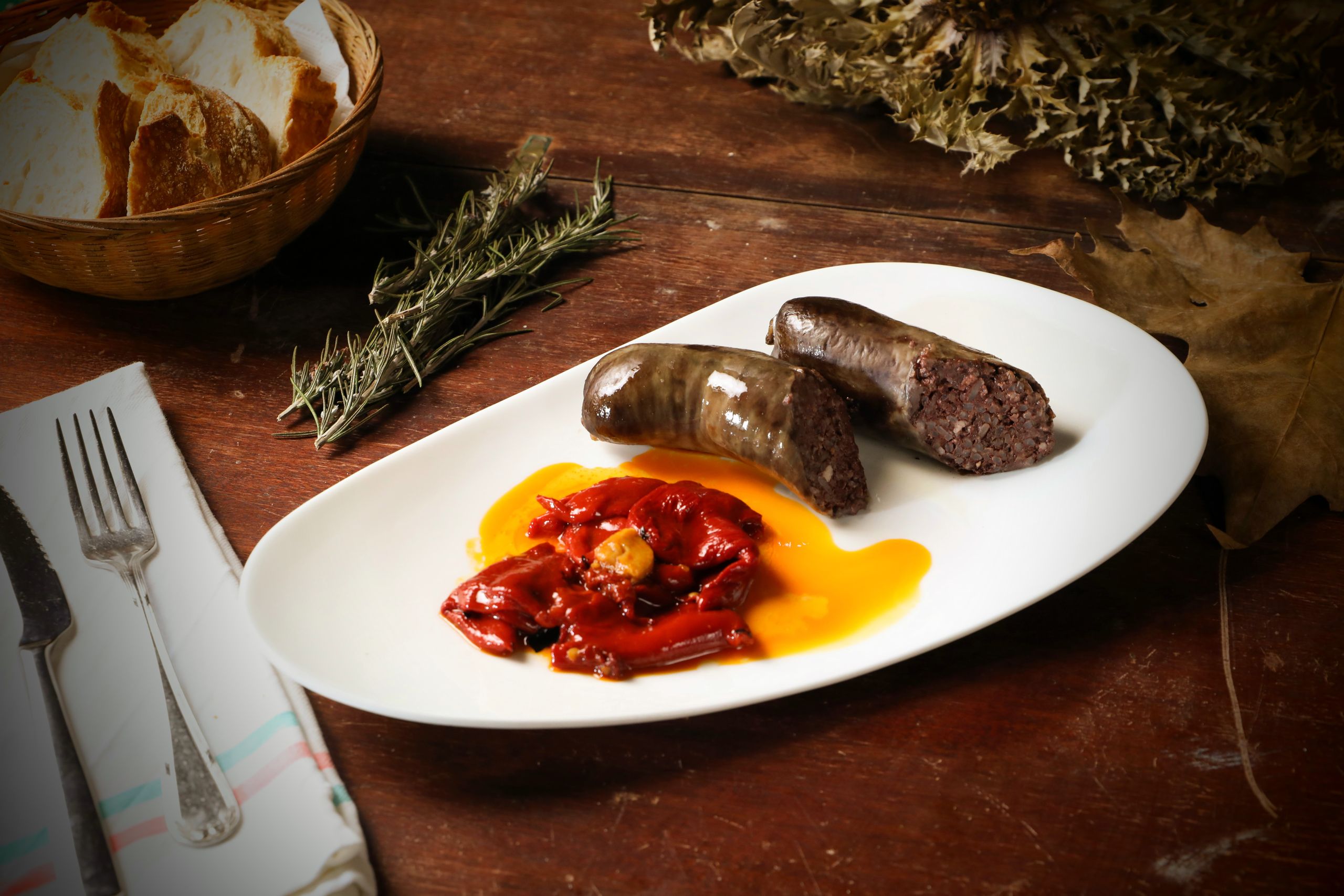 A rustic presentation of blood sausage with roasted red peppers and bread on a wooden table.