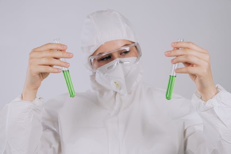 A scientist in protective gear observing green liquids in test tubes, demonstrating laboratory safety.