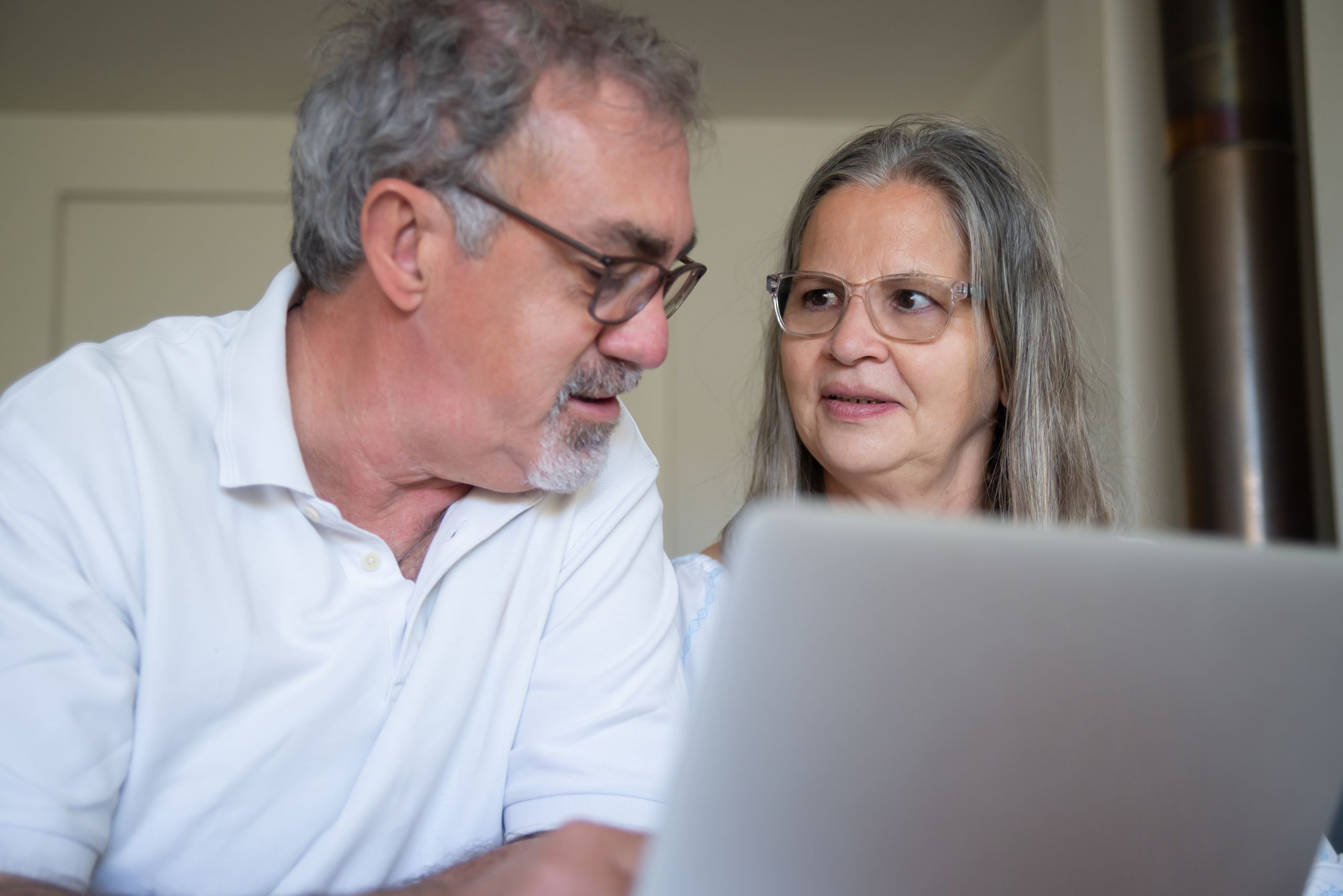 A senior couple engaging with technology at home, discussing content on a laptop.