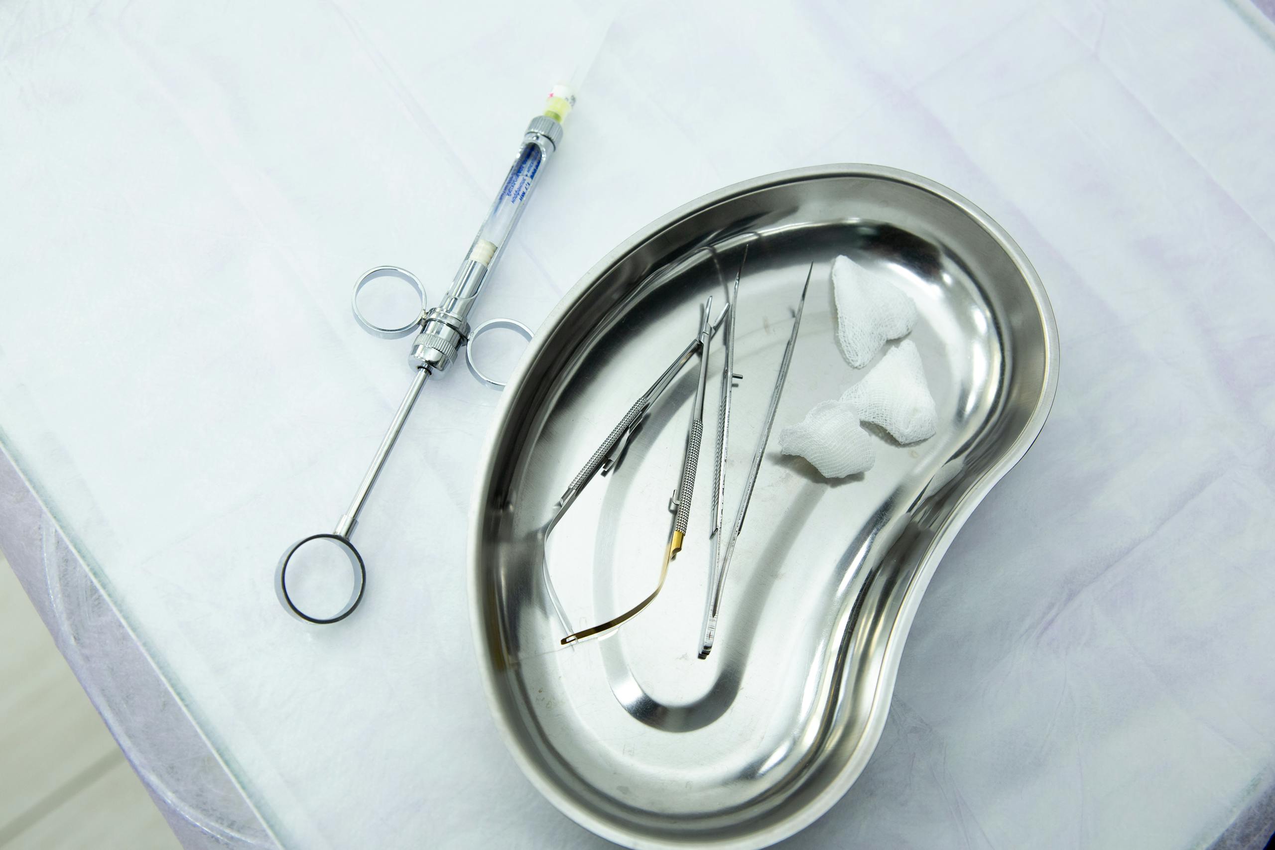 A set of sterile medical tools and syringe displayed in a kidney tray for dental or surgical use.