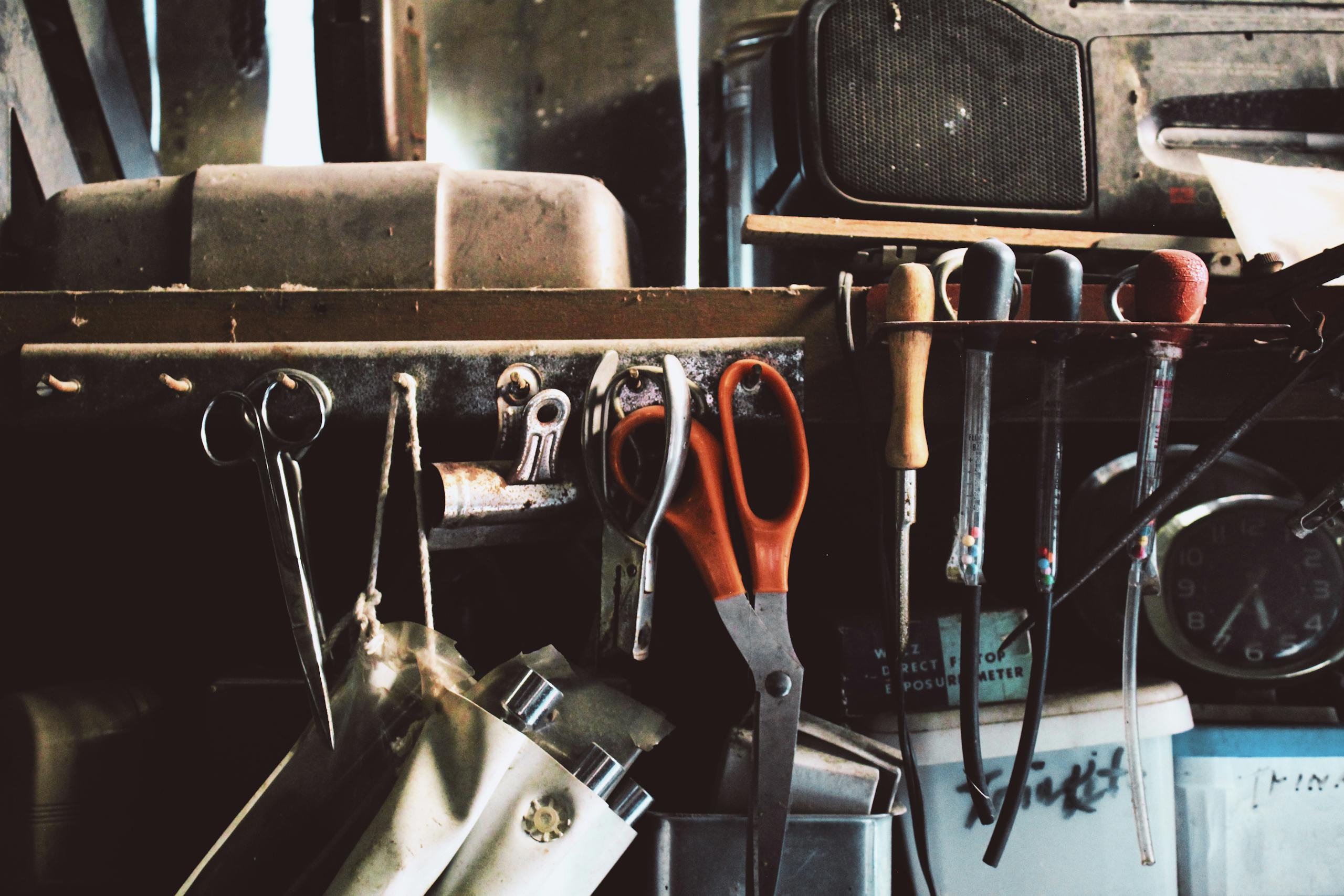 A shelf in a workshop holding tools like scissors, screwdrivers, and more.