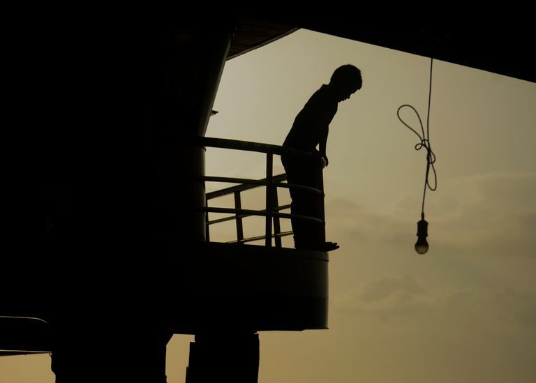 A silhouette of a person standing on a balcony at sunset with a hanging light bulb in view.