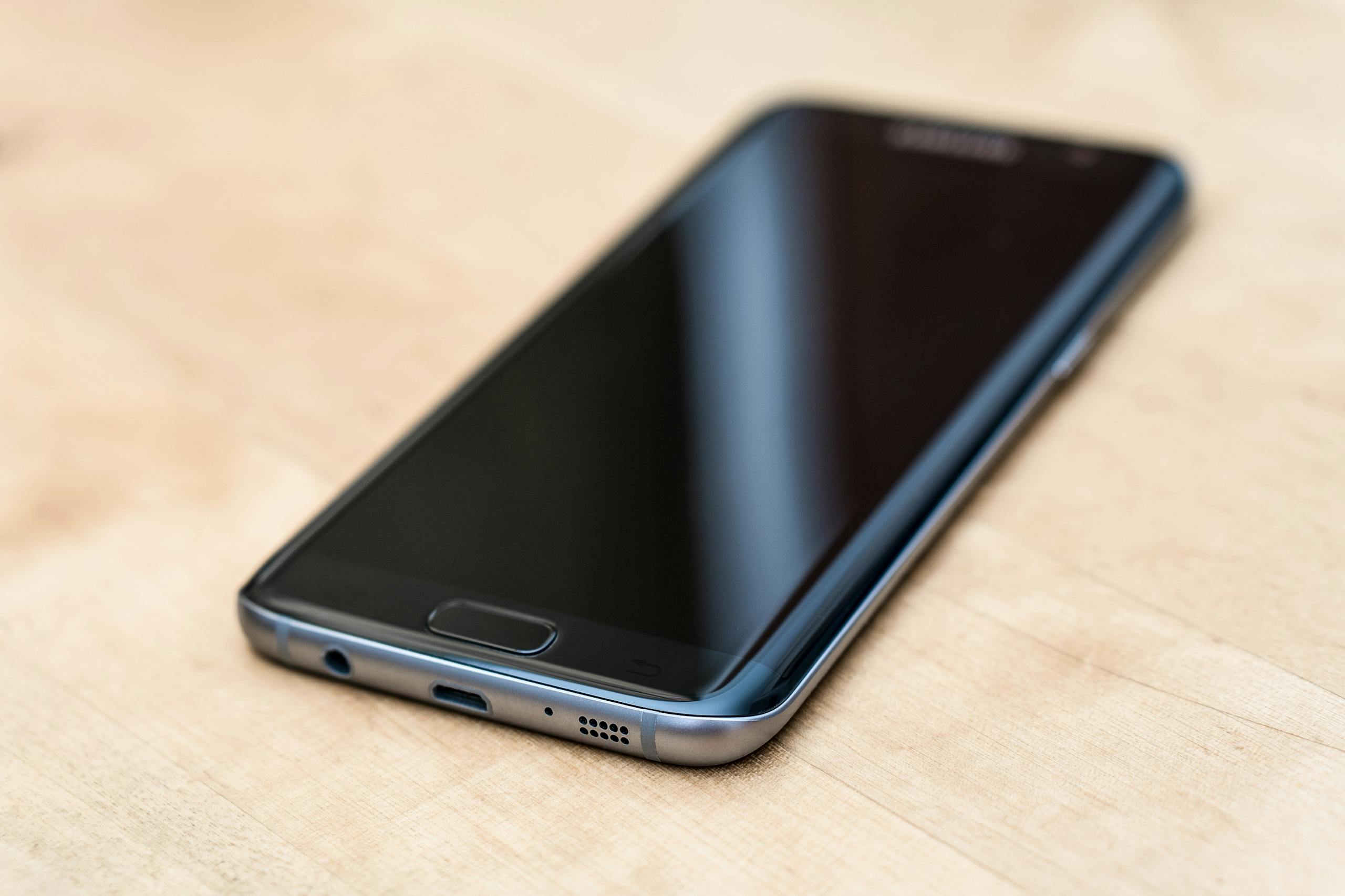 A sleek modern smartphone placed on a wooden surface, showcasing technology design.