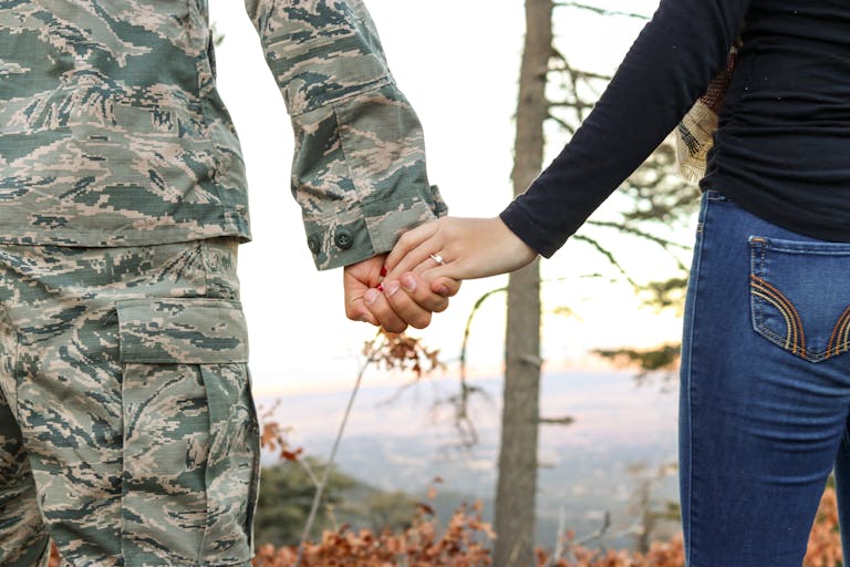 A soldier in uniform holding hands with a woman showing her engagement ring outdoors.