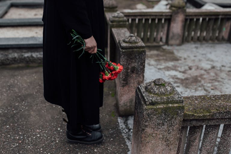 A somber scene of a person holding red flowers near a tombstone at a cemetery.