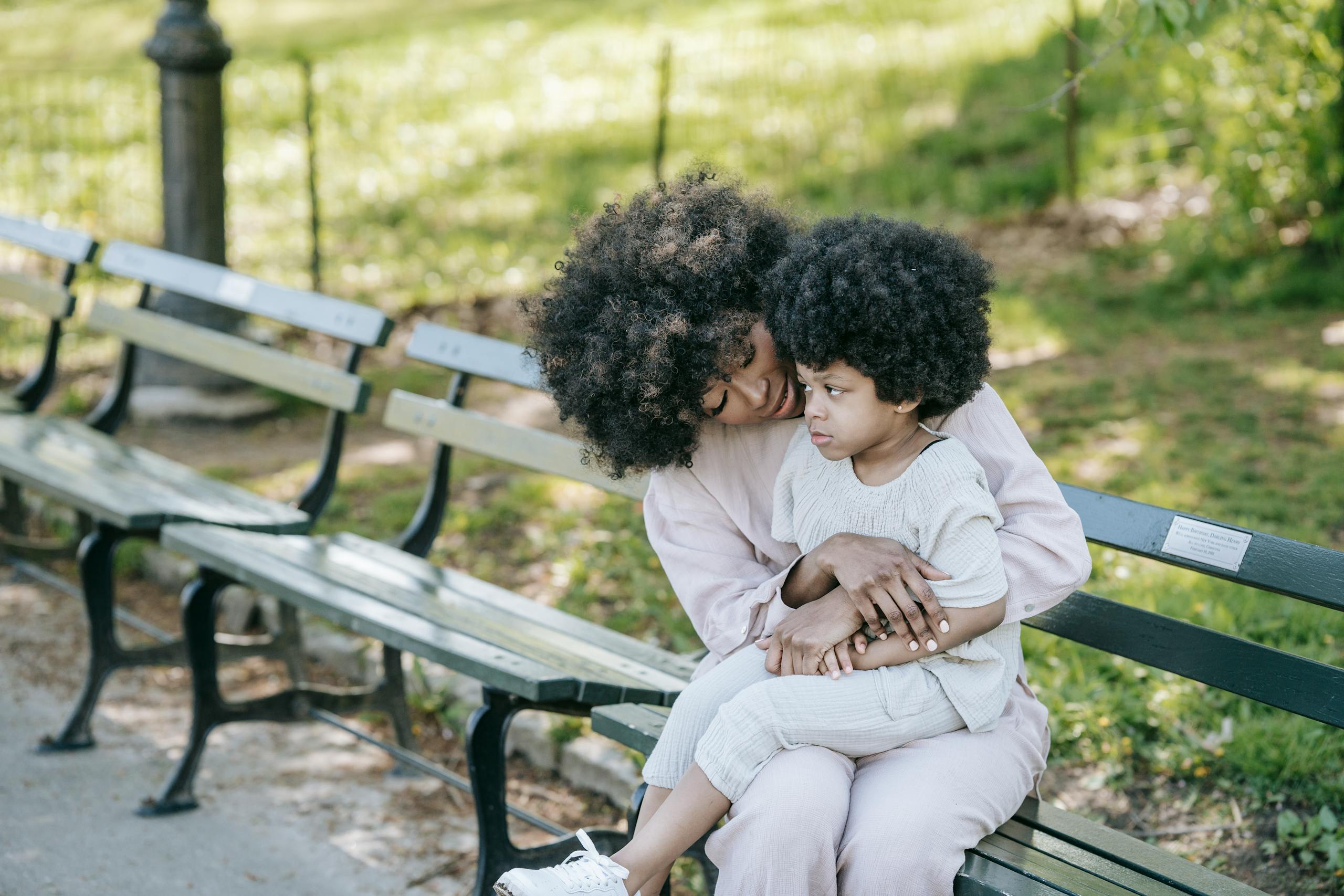 A tender moment between mother and child sitting on a park bench in spring.