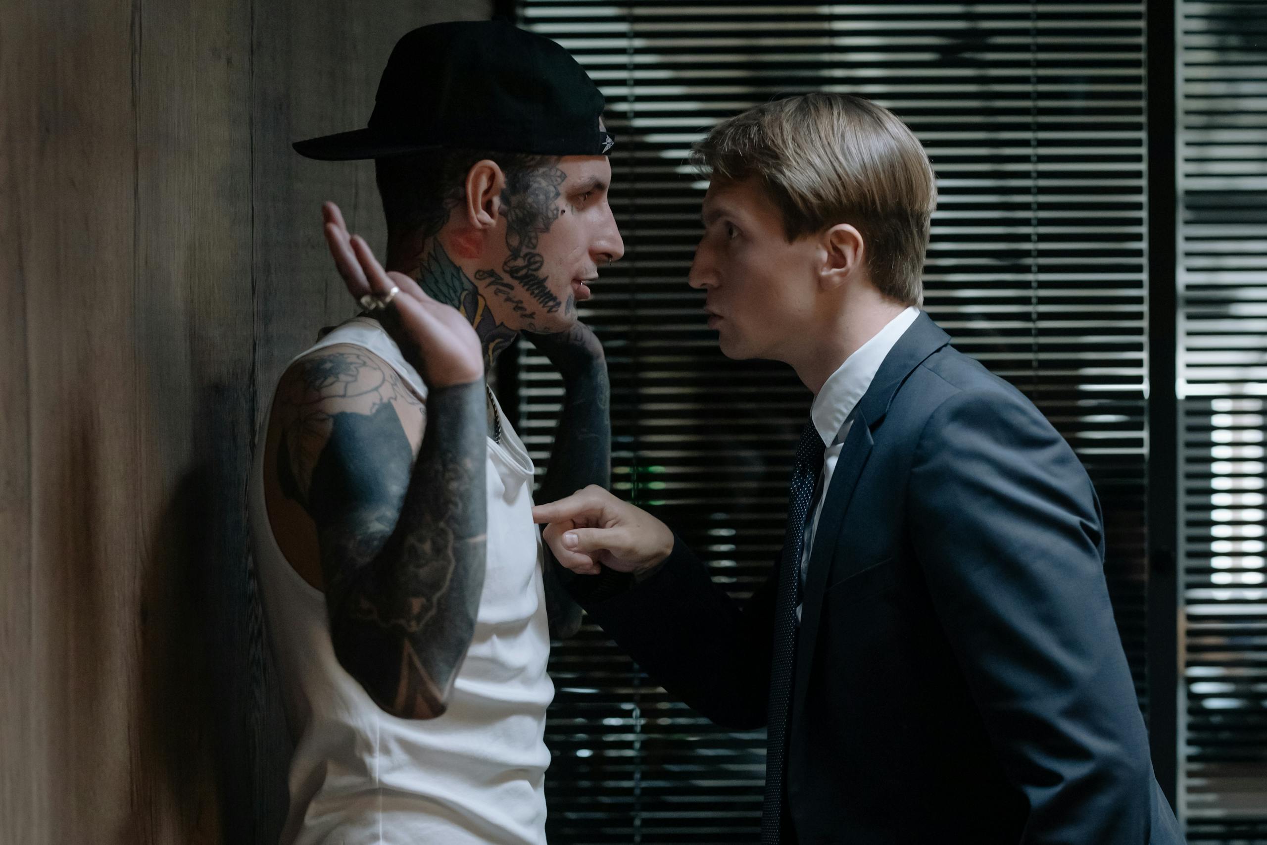 A tense indoor scene depicting an intense interrogation confrontation between two men.