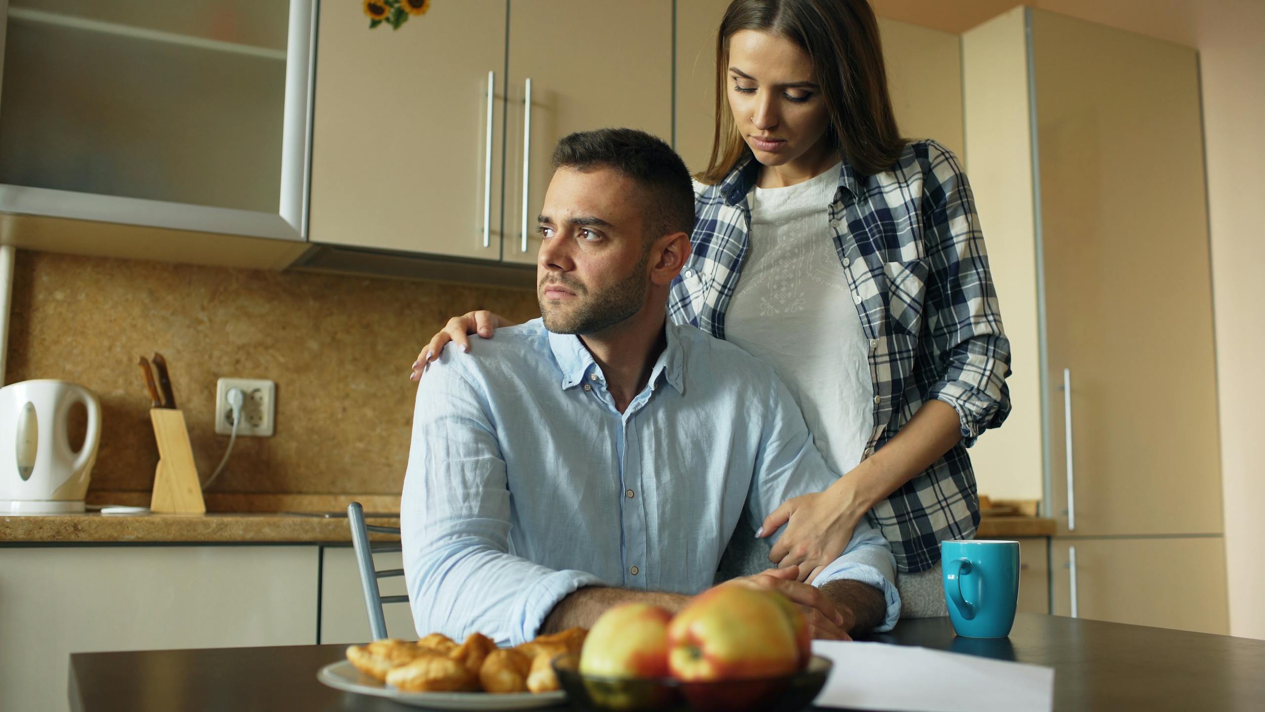 A thoughtful couple shares an emotional moment in a cozy kitchen setting.