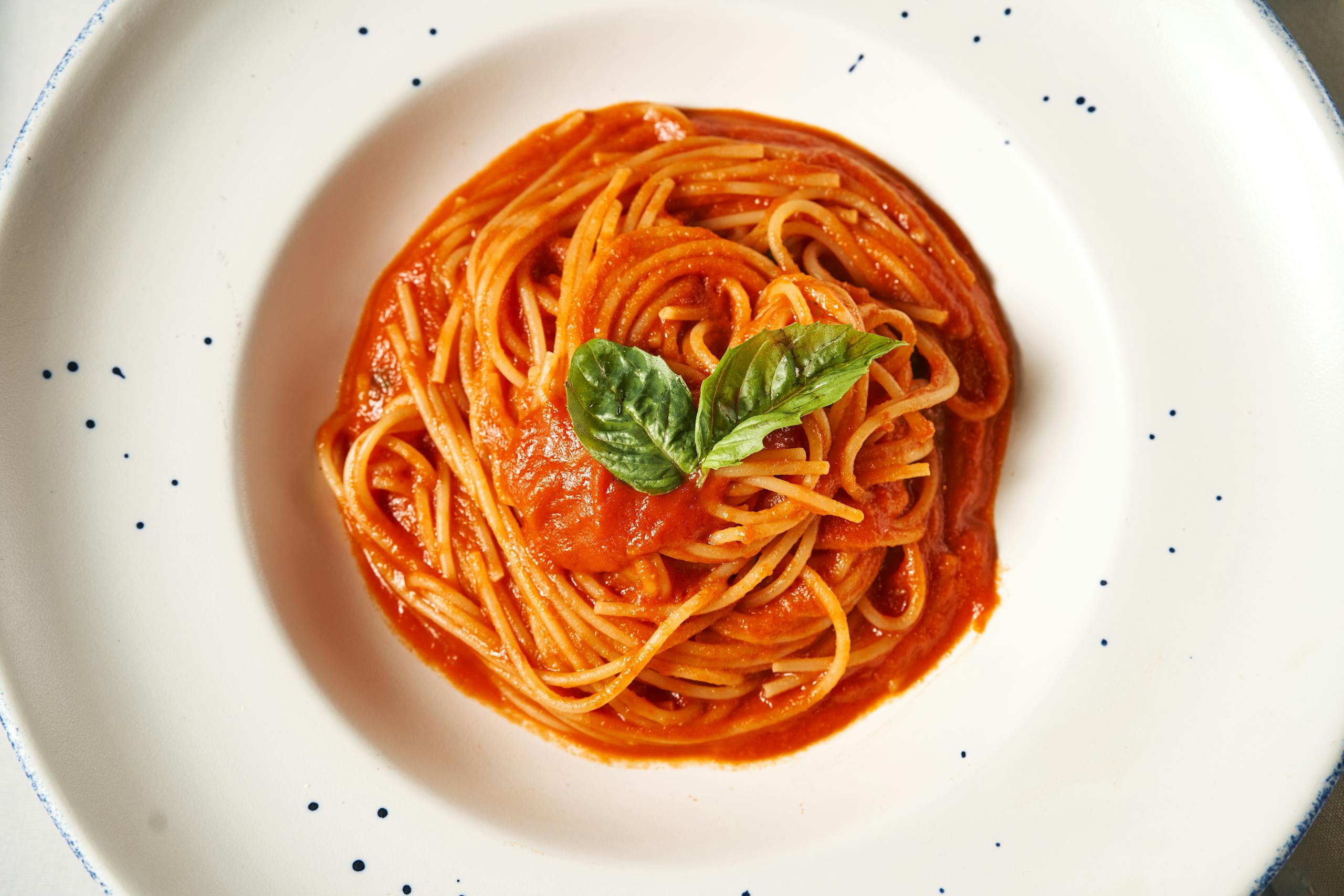 A top-down view of a plate of spaghetti with rich tomato sauce and fresh basil garnish.