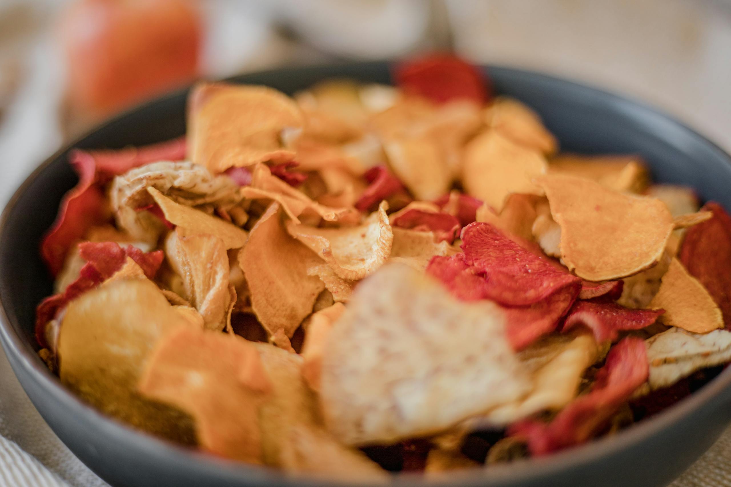 A vibrant assortment of vegetable chips in a black bowl, perfect for snack lovers.