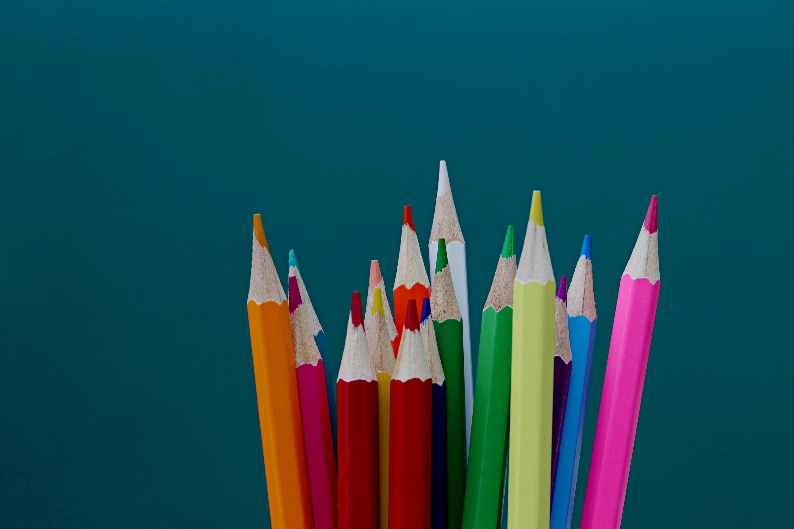A vibrant collection of sharpened color pencils arranged against a teal background.