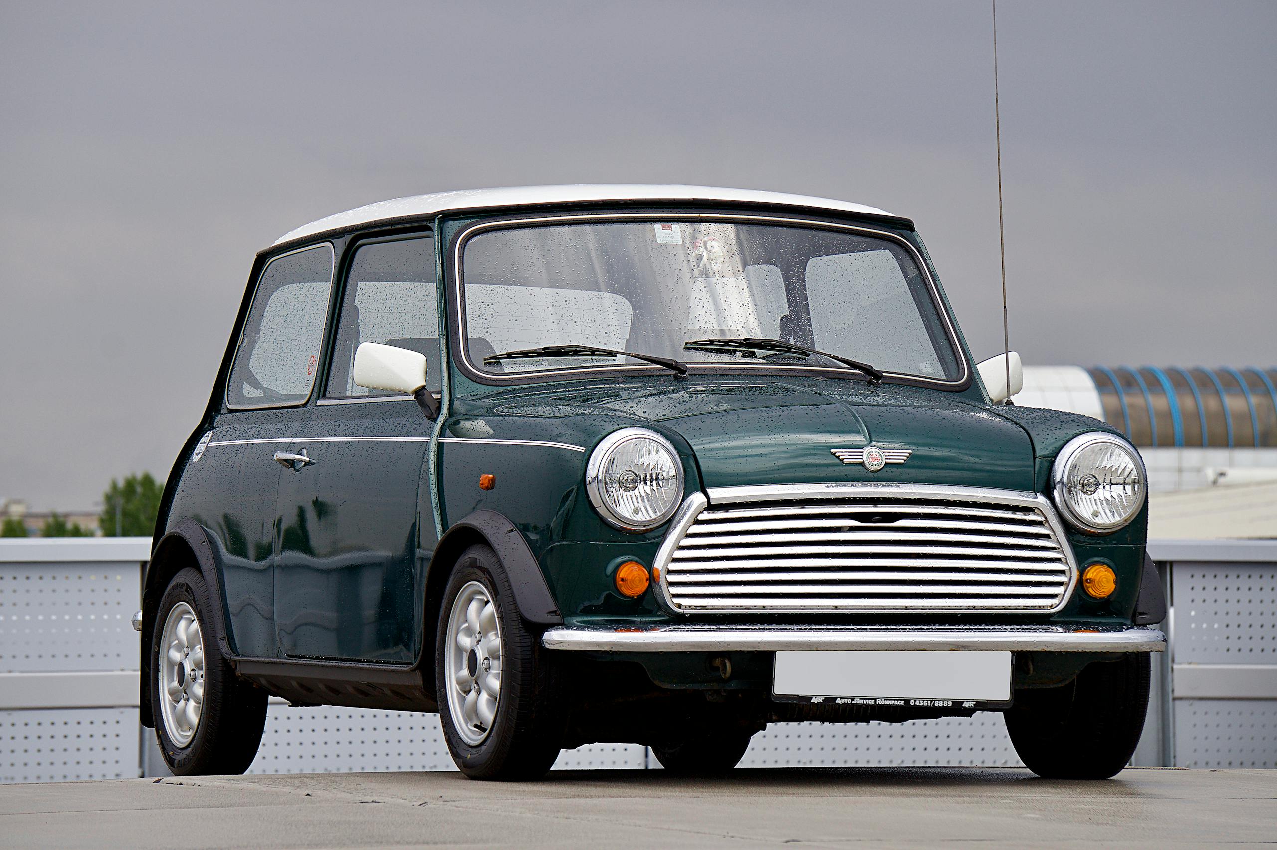 A vintage green Mini Cooper parked in a modern urban area, showcasing its classic design.